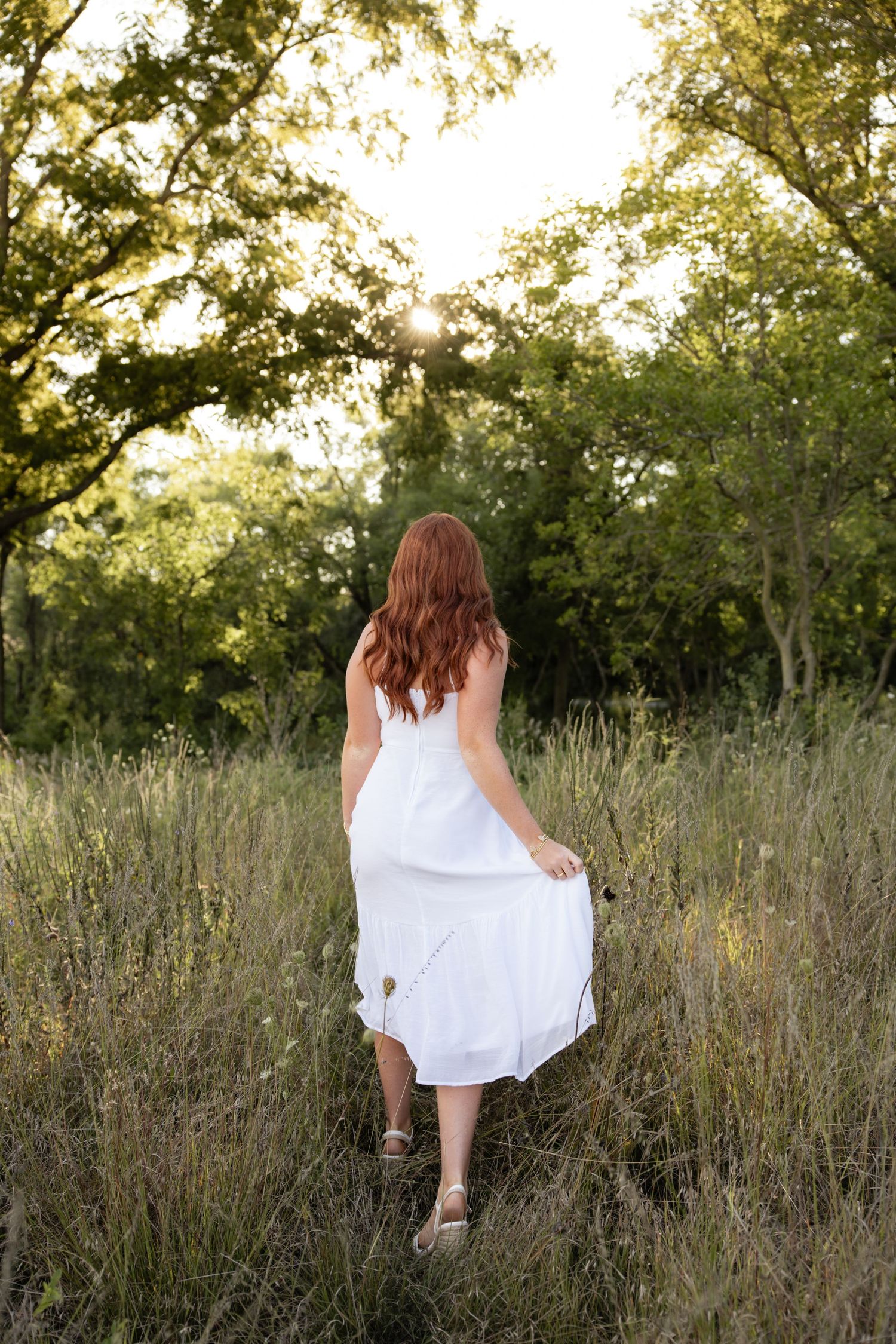 A woman in flowing white dress walks through a wild meadow at golden hour.