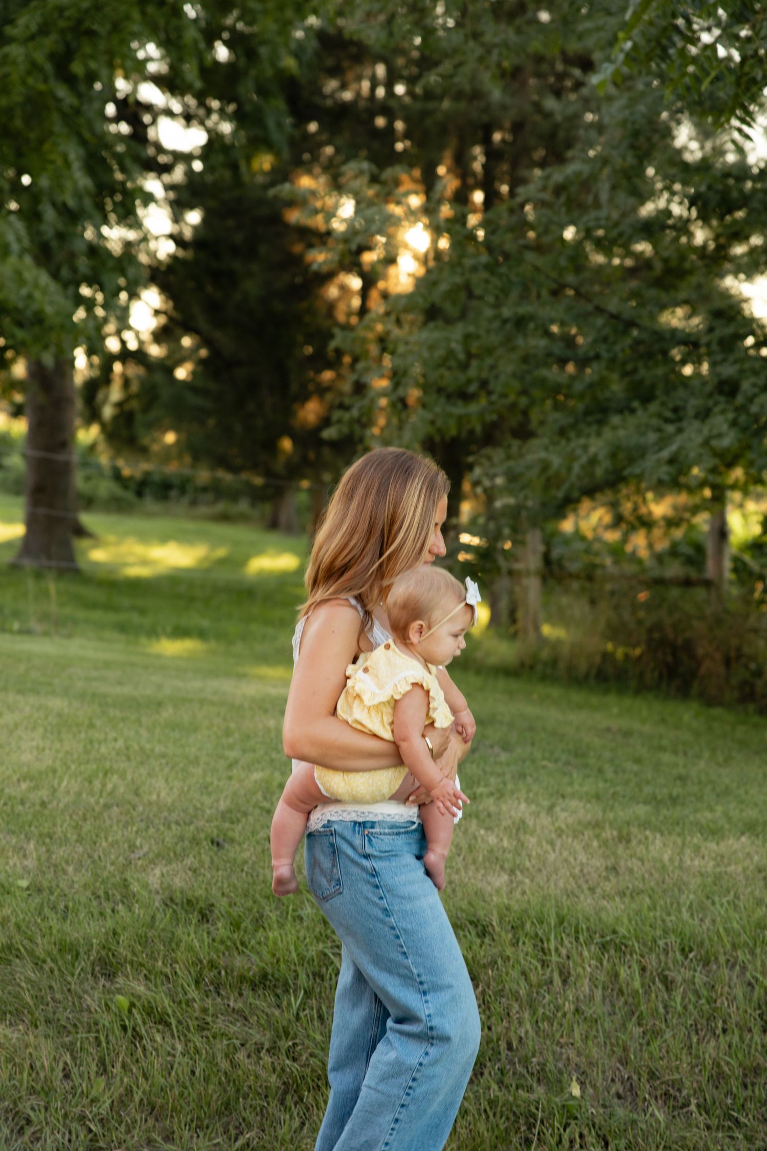 Woman in denim holding child outdoors during golden hour.