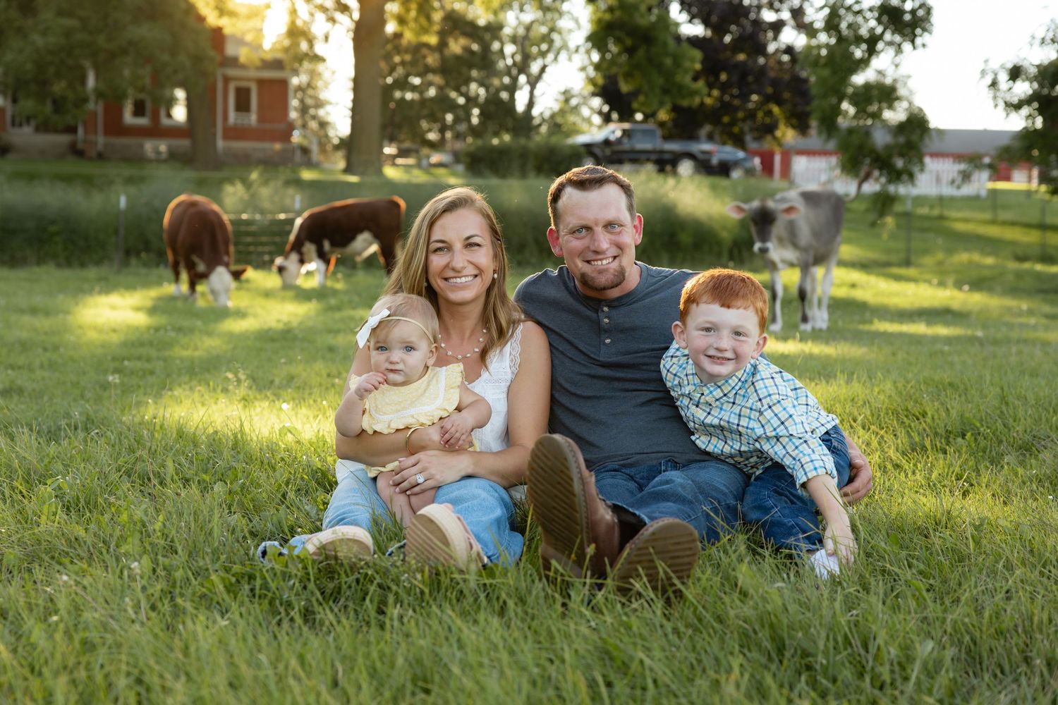 Family lounging on grass with trees and sunset in background.