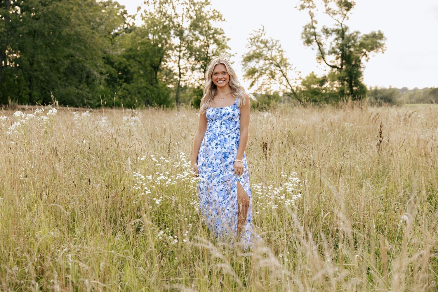 A person wearing a blue floral dress stands in a summer meadow with wildflowers.