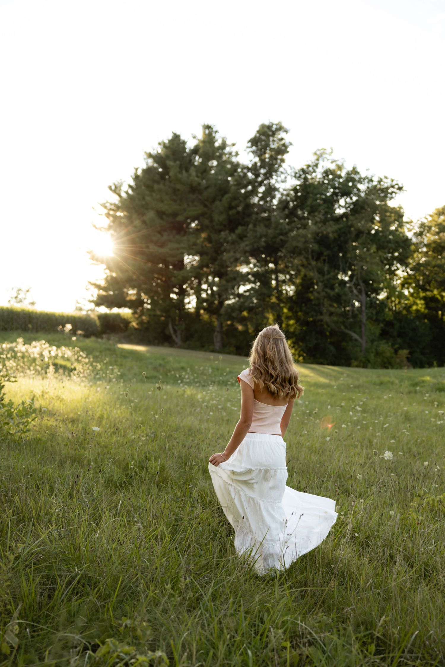Person in white dress twirling in a sunlit meadow during golden hour.