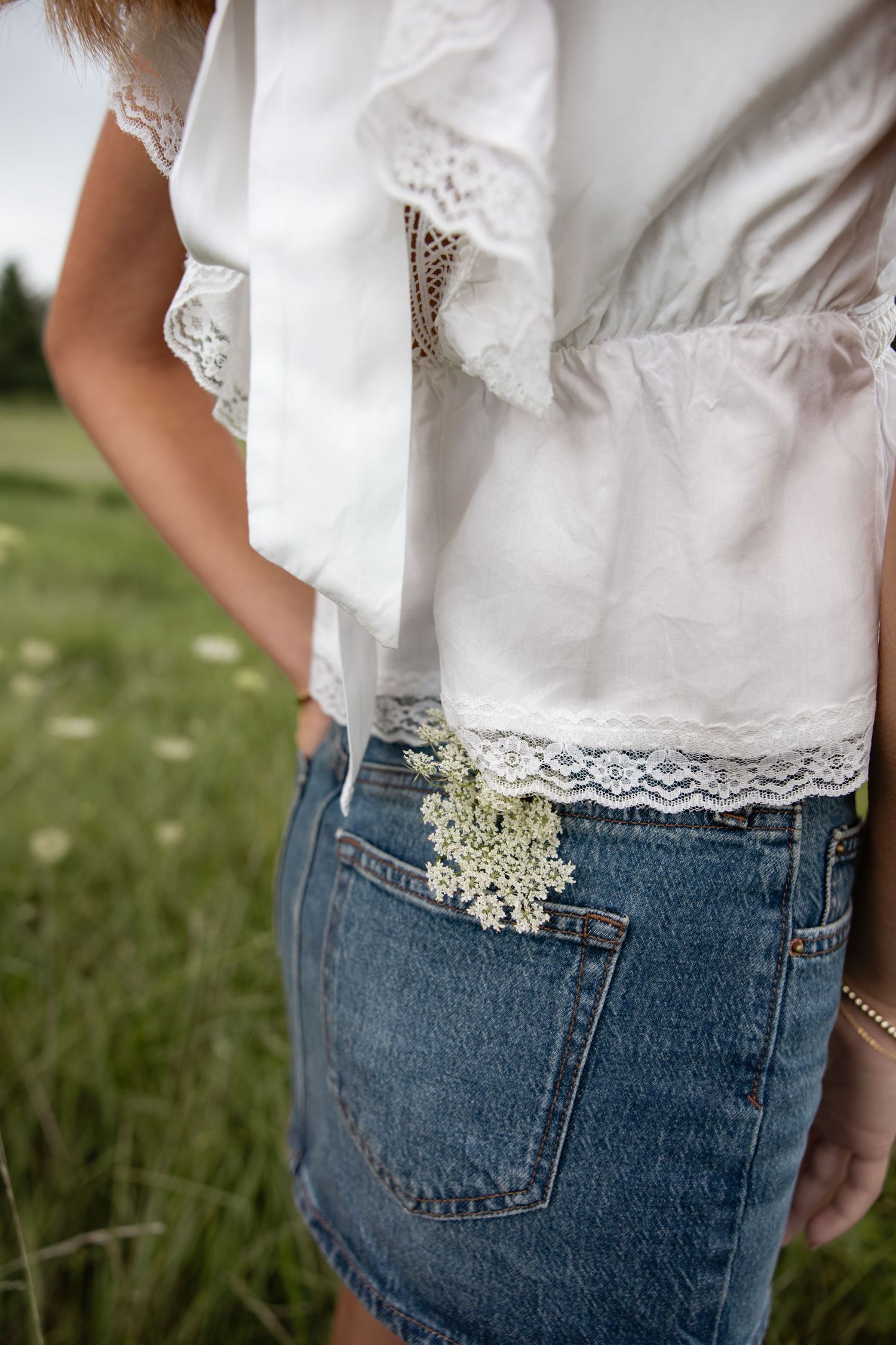 Detail shot of white lace top and denim with delicate wildflowers tucked in pocket.