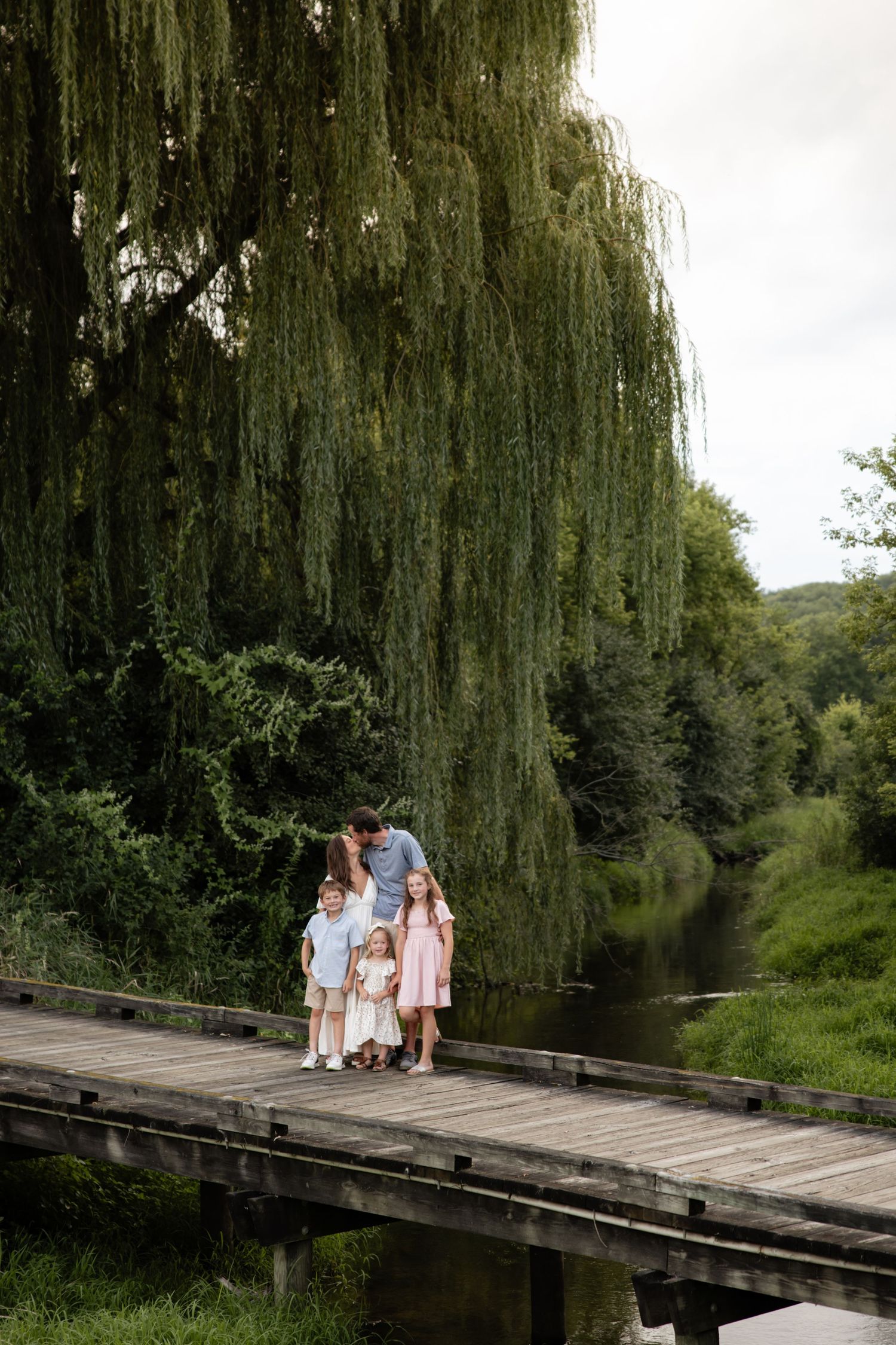 Family standing together on a wooden bridge under a dramatic weeping willow tree.