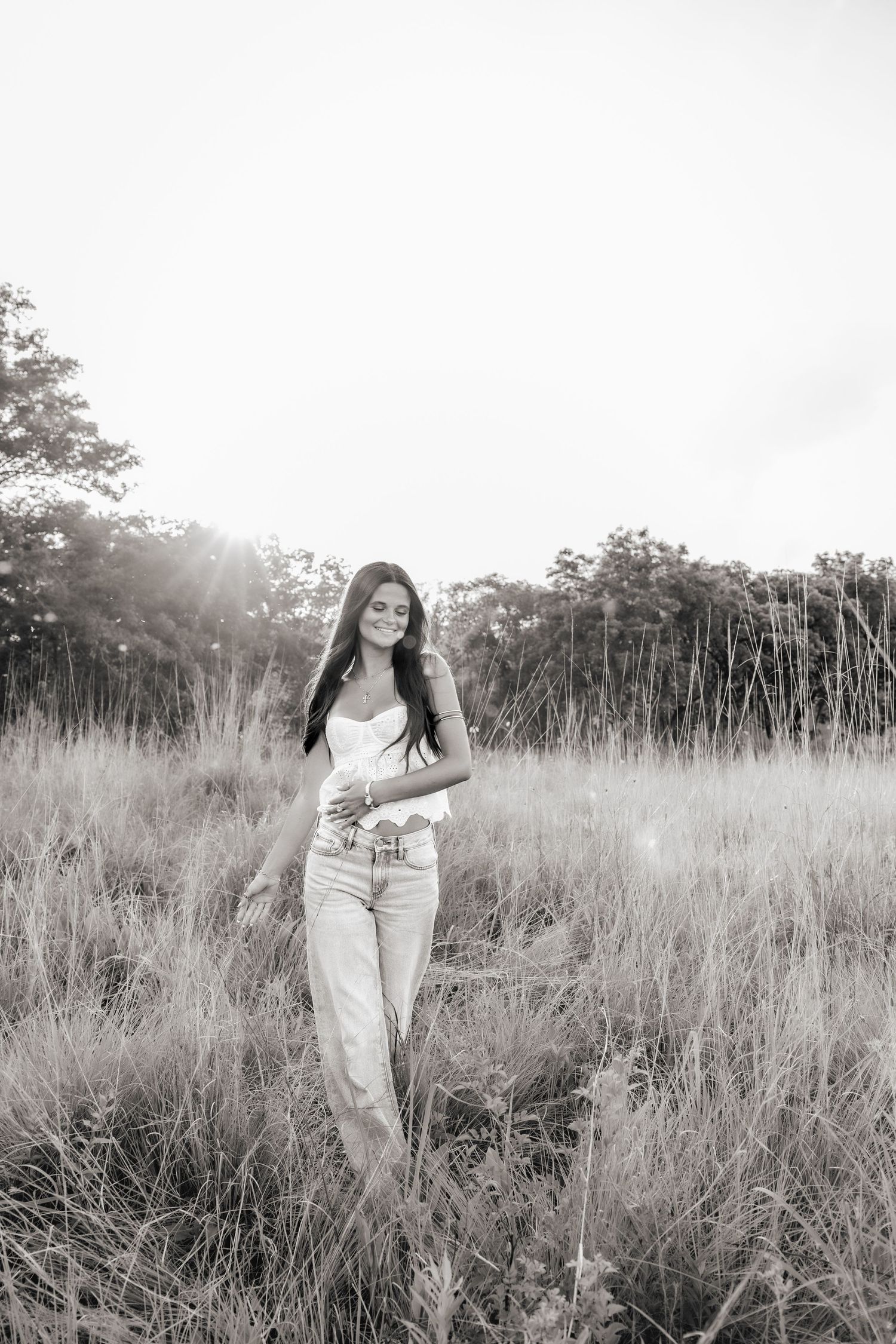 Black and white portrait series of a person in white clothing walking through a sunlit meadow of tall grass.