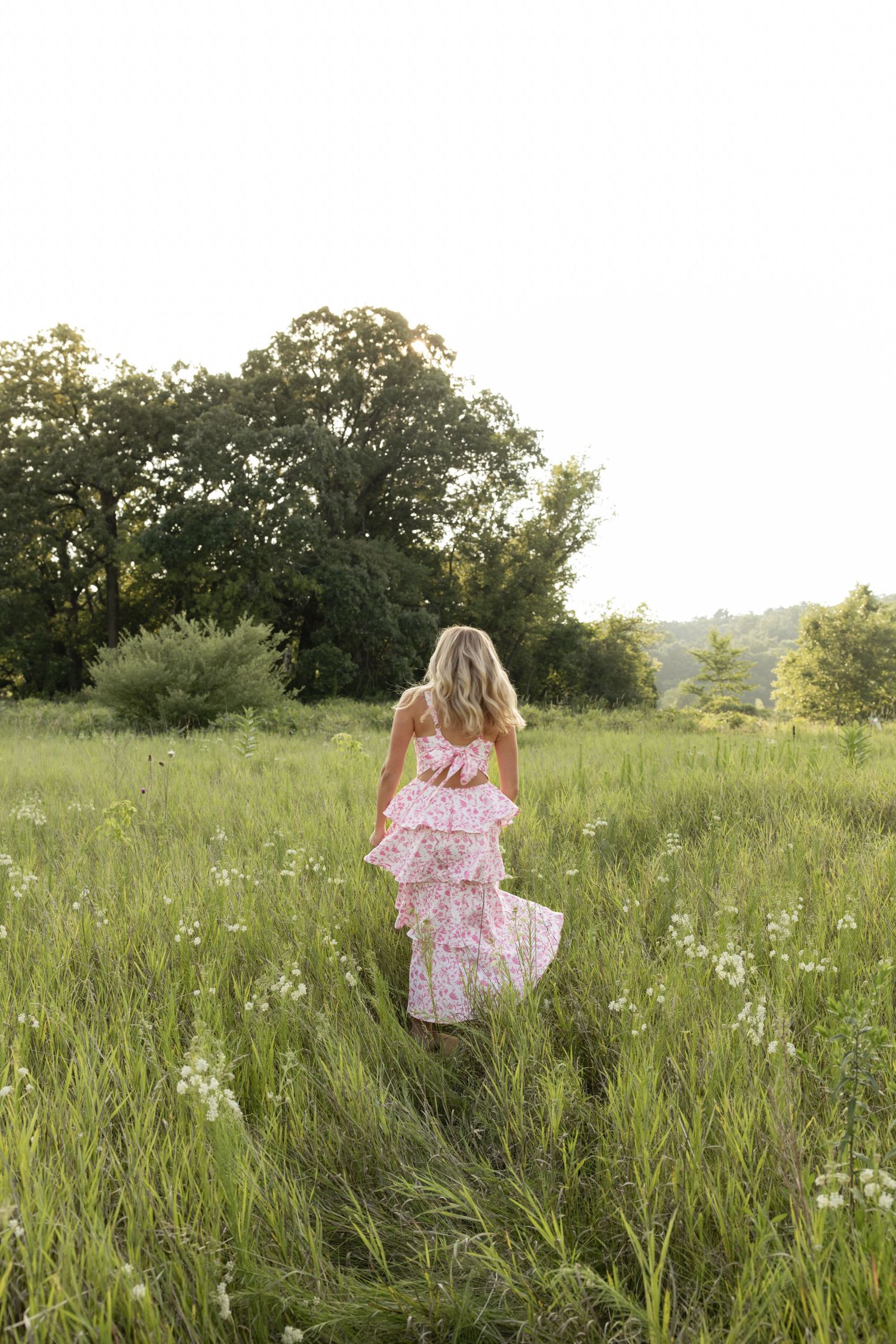 Person in floral dress walking through tall grass and wildflowers at sunset.