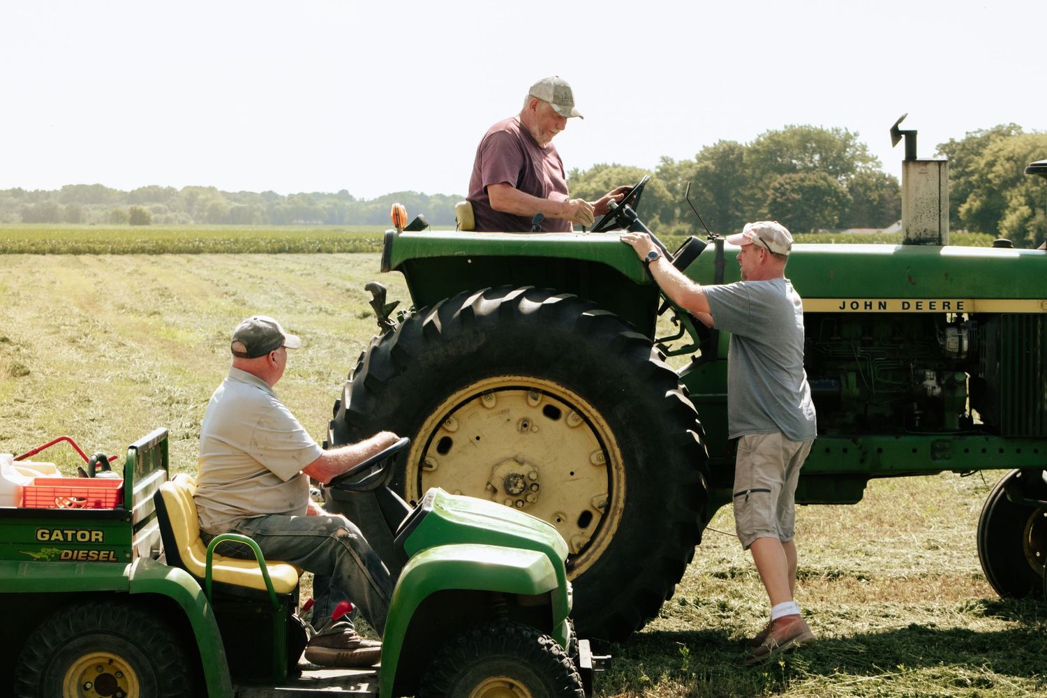 Green tractors and farm equipment lined up in a field during agricultural operations.