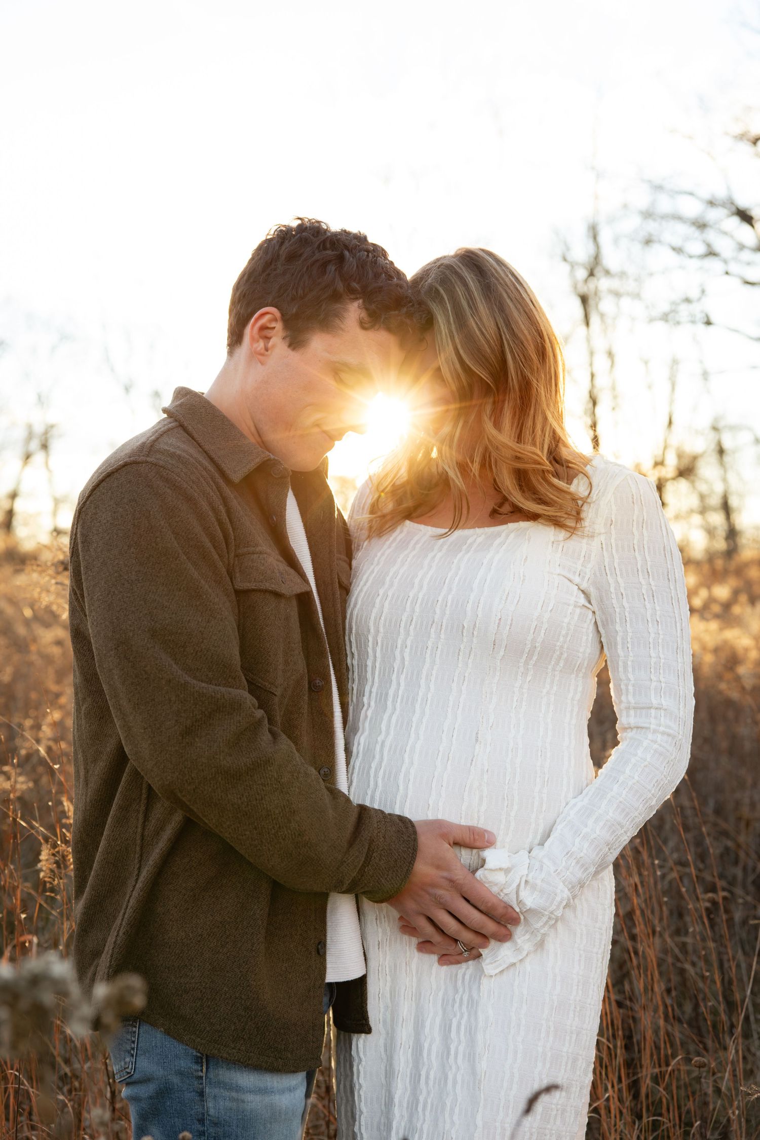 Maternity photos at sunset with couple embracing in field.
