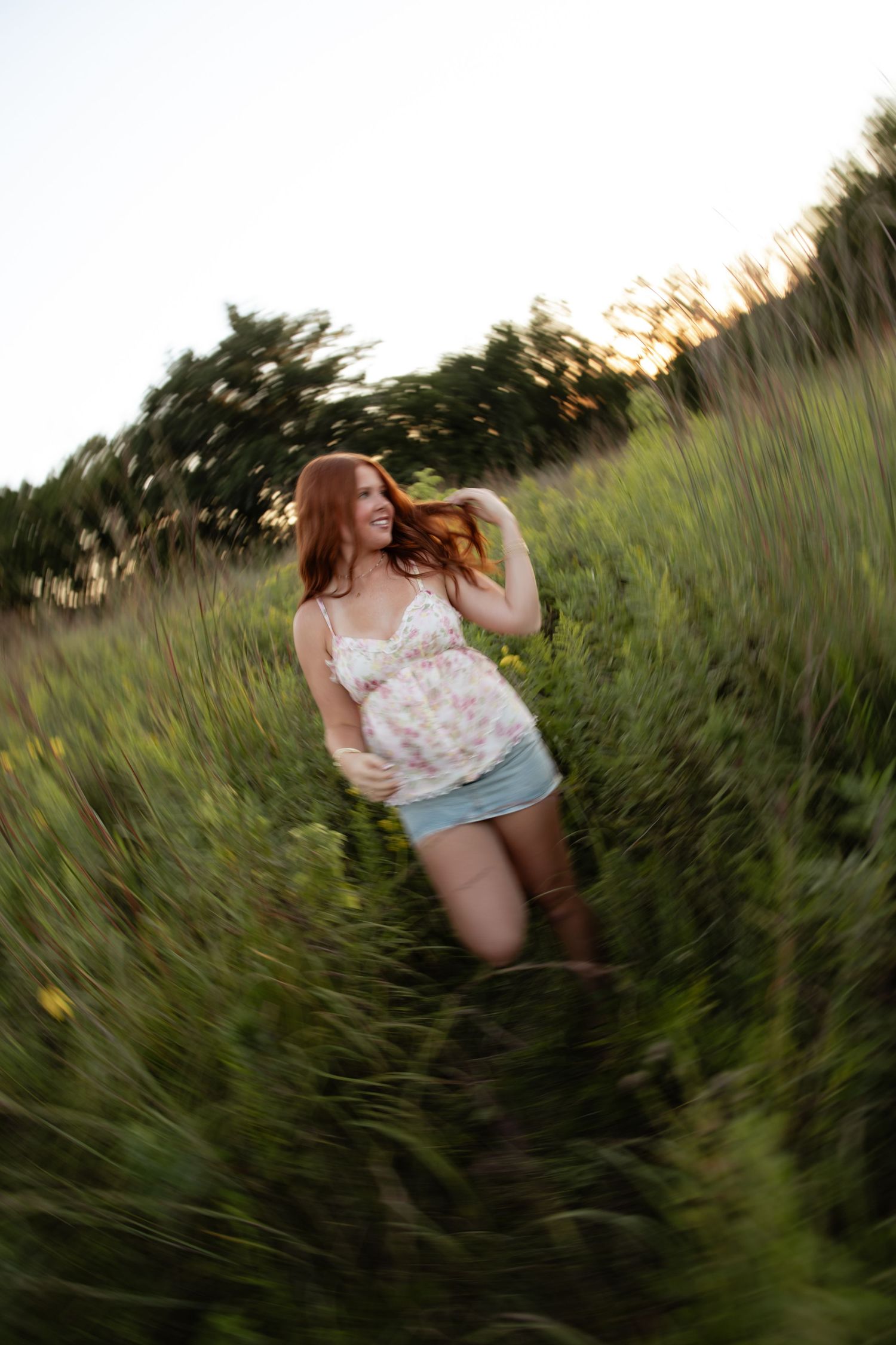 Person in a white floral dress twirling joyfully in a sunlit meadow during golden hour.