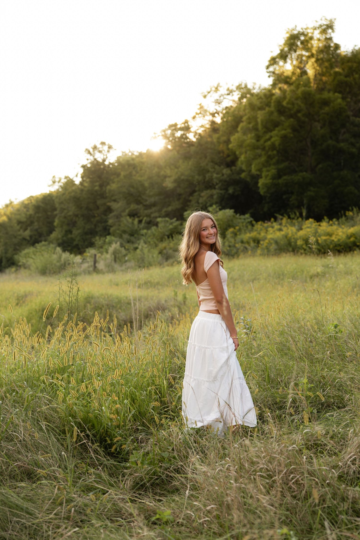 A woman in a white dress twirls in a sunlit meadow during golden hour.