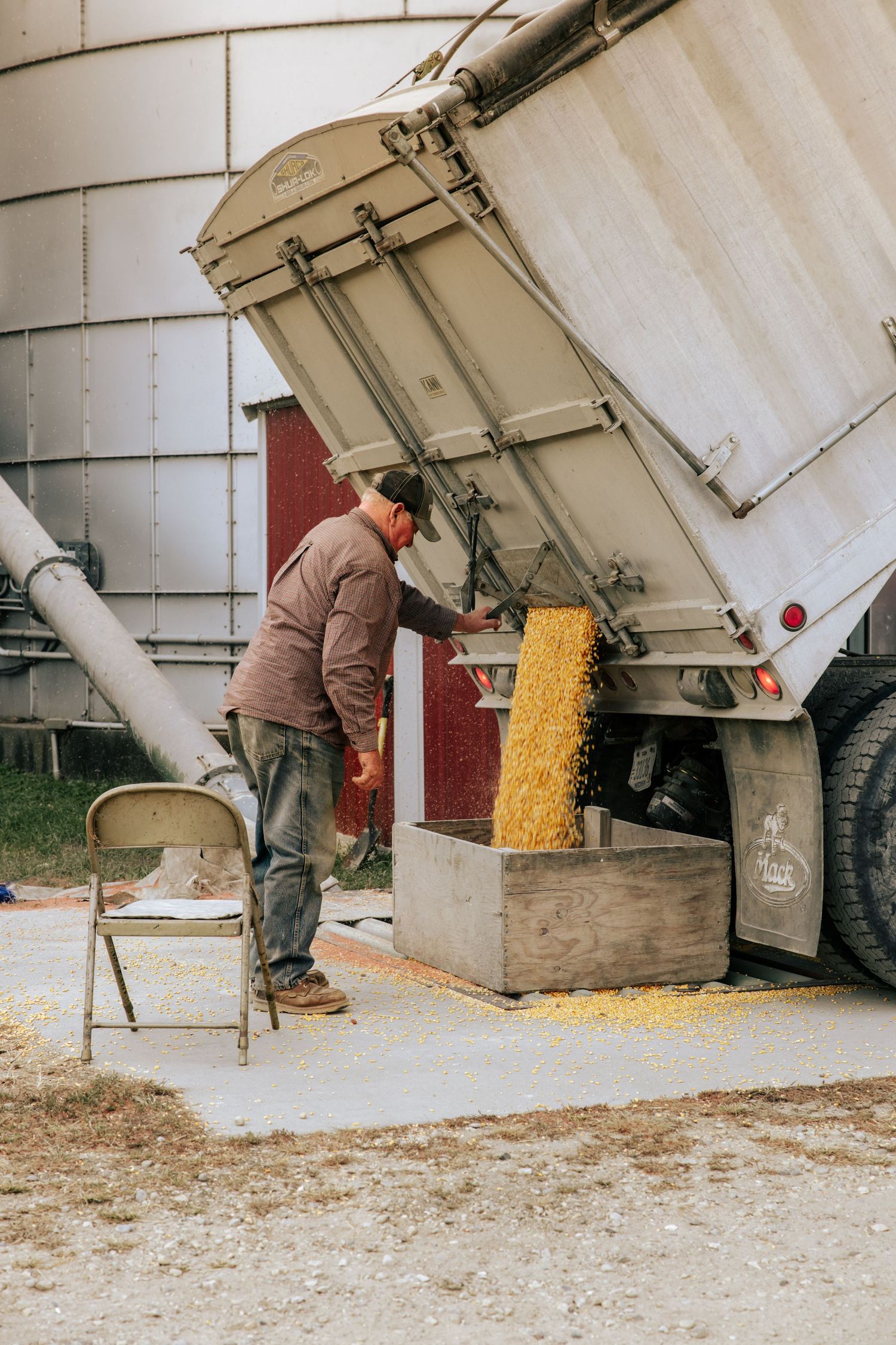 Worker unloading grain from a large white storage container into wooden boxes on the ground.