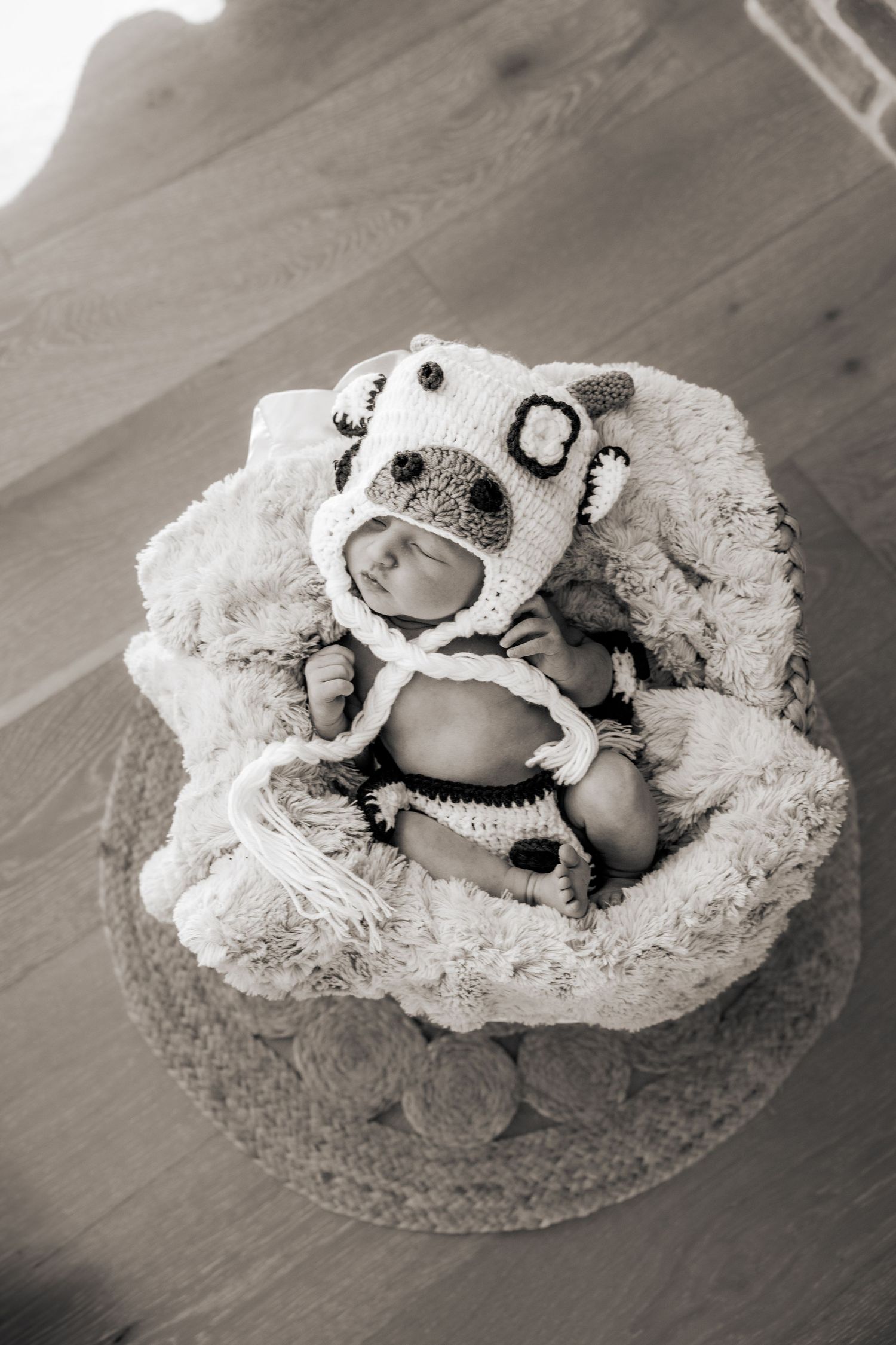 A series of black and white photos showing a baby sleeping in a white crochet blanket on a hardwood floor.