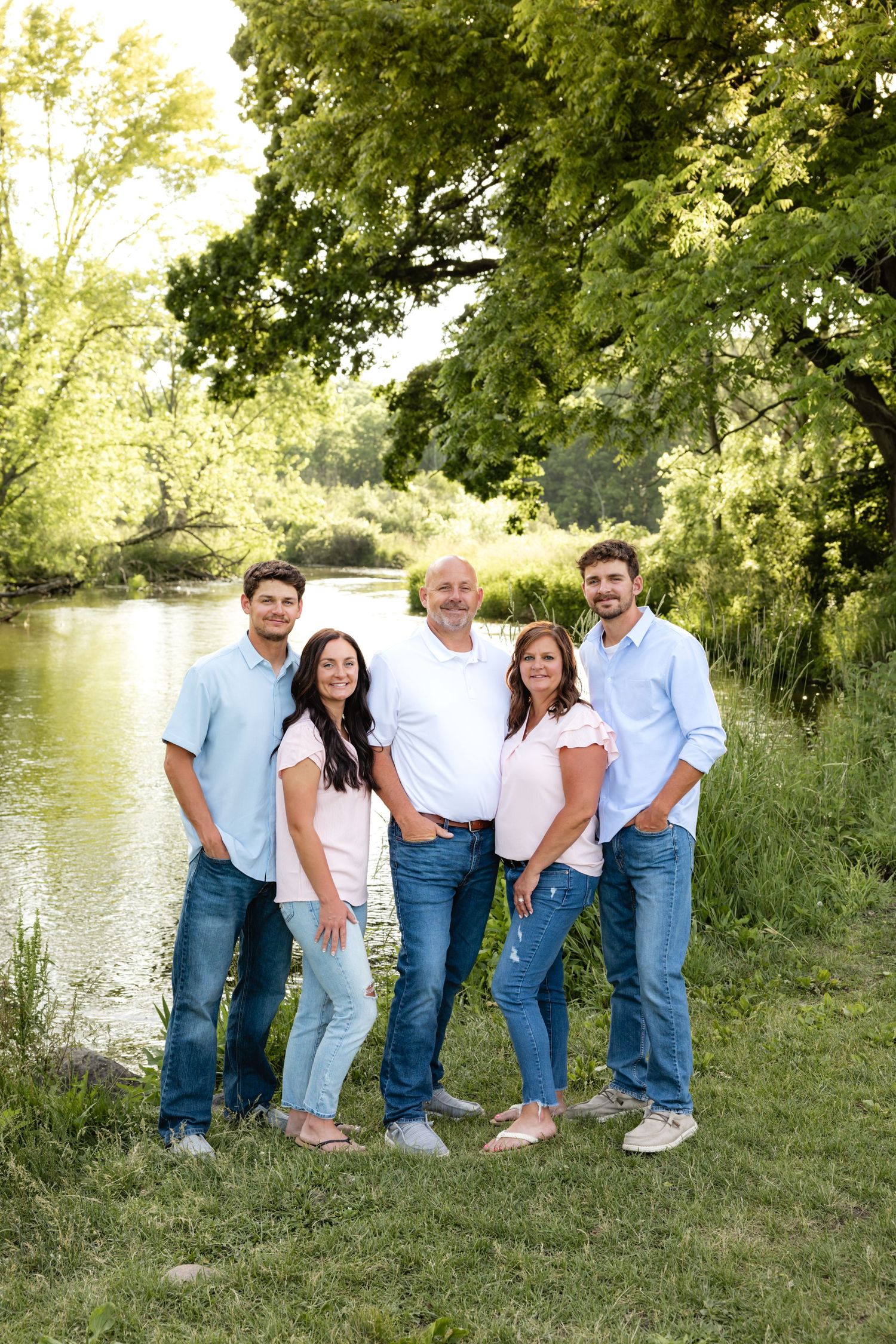 Group portrait by a lake with matching denim and white shirts in natural setting.