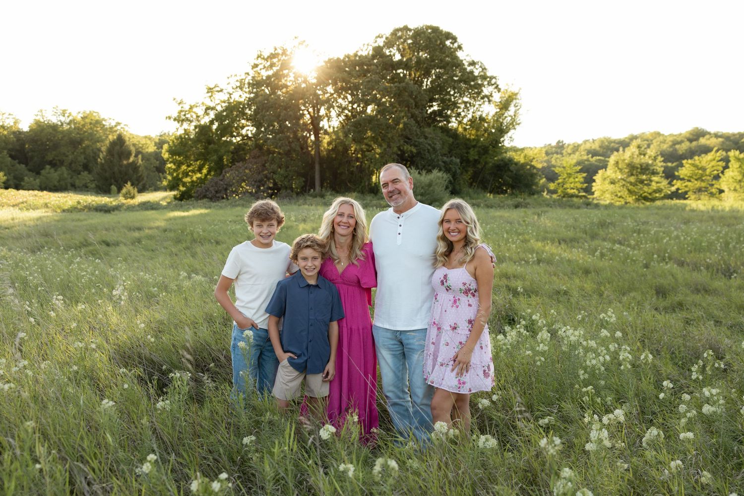 Family group portrait in a wildflower meadow at sunset with trees in background.