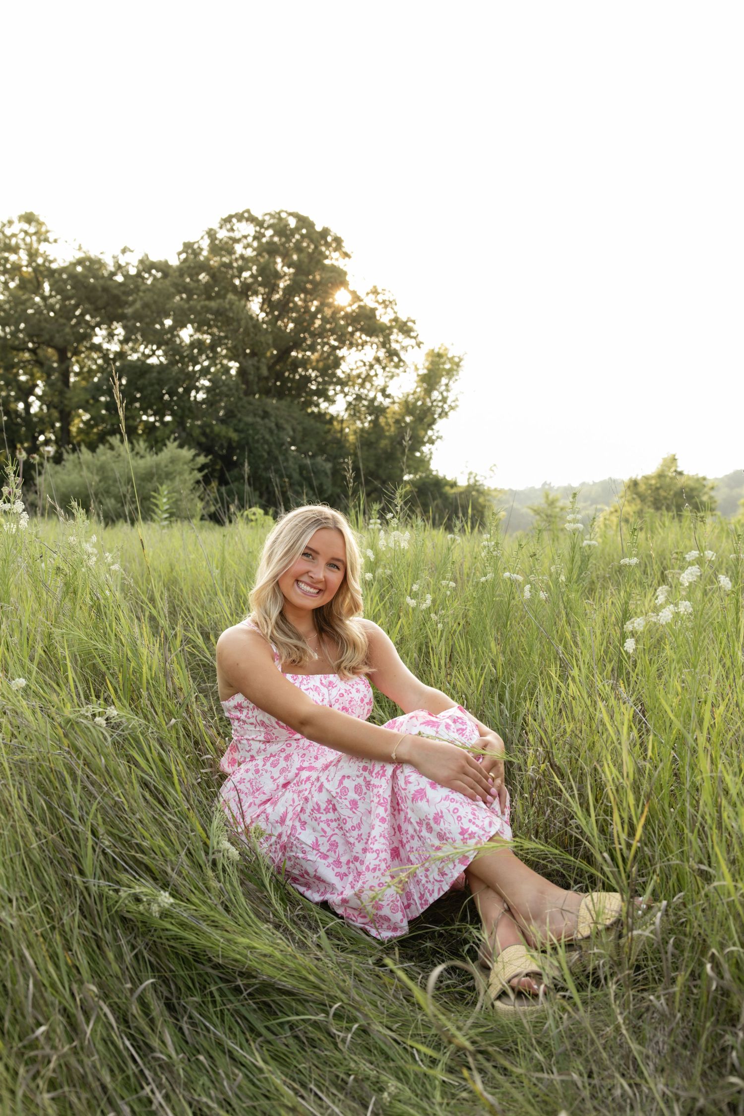 Person in a floral dress relaxing in tall summer grass during sunset.