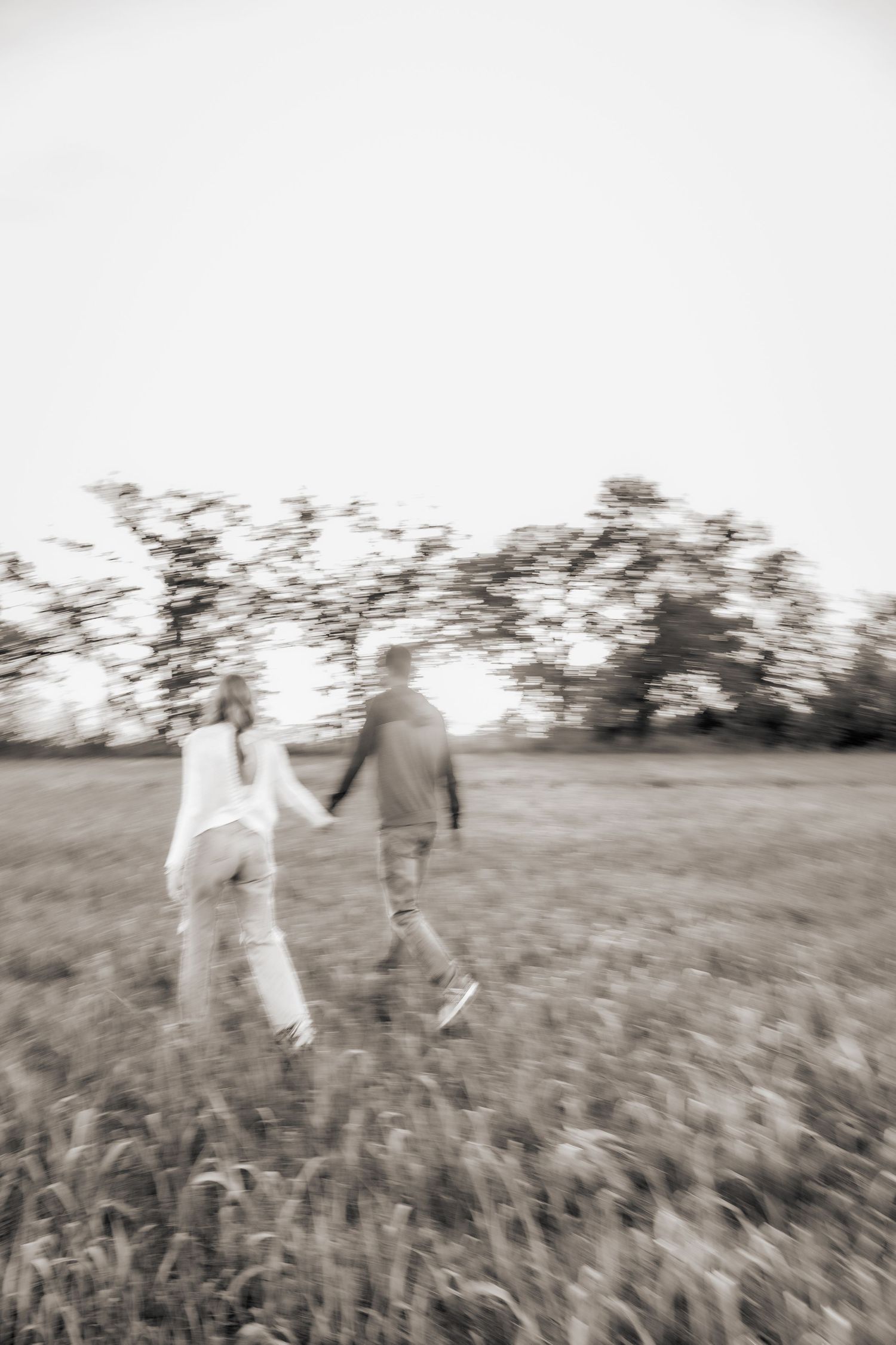 Black and white image of two people walking together through a grassy field.