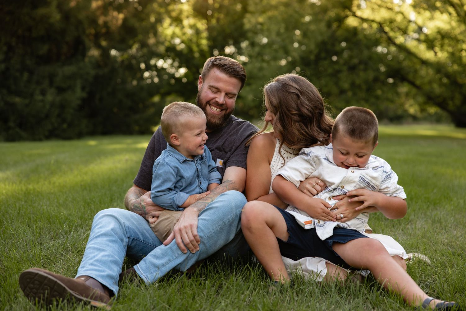 Family sharing tender moments while lying in green summer grass.
