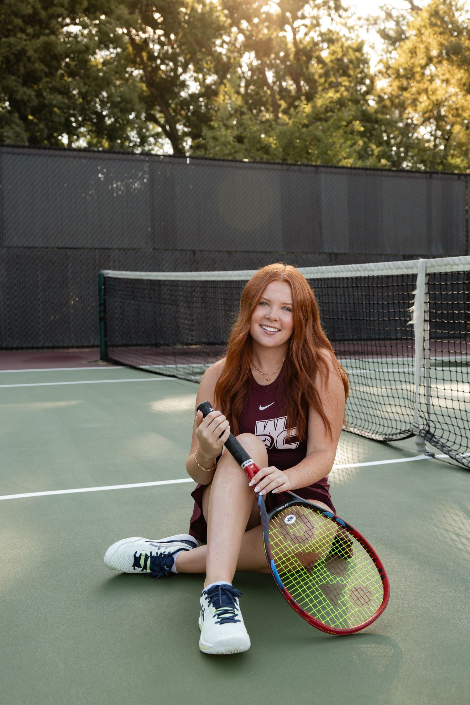 Person relaxing on a tennis court with a racket and tennis balls at dusk.