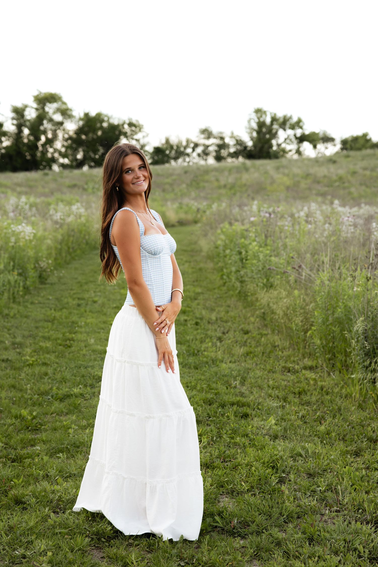 A woman in a flowing white dress poses in a wildflower meadow during golden hour.