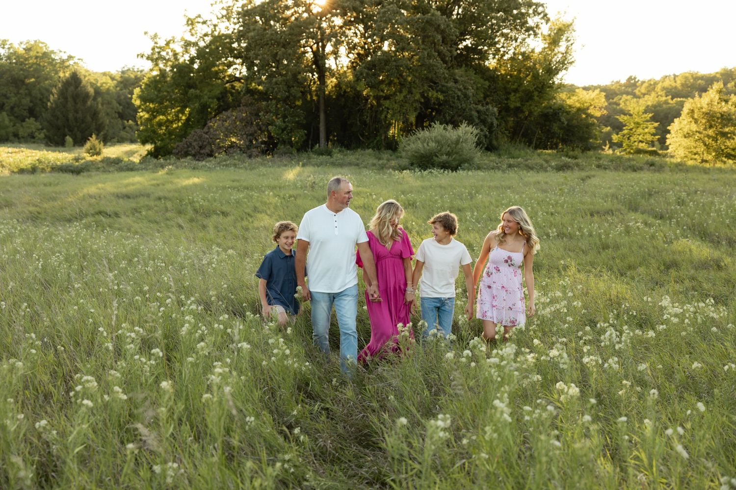 Family walking together through a meadow filled with white wildflowers at sunset.