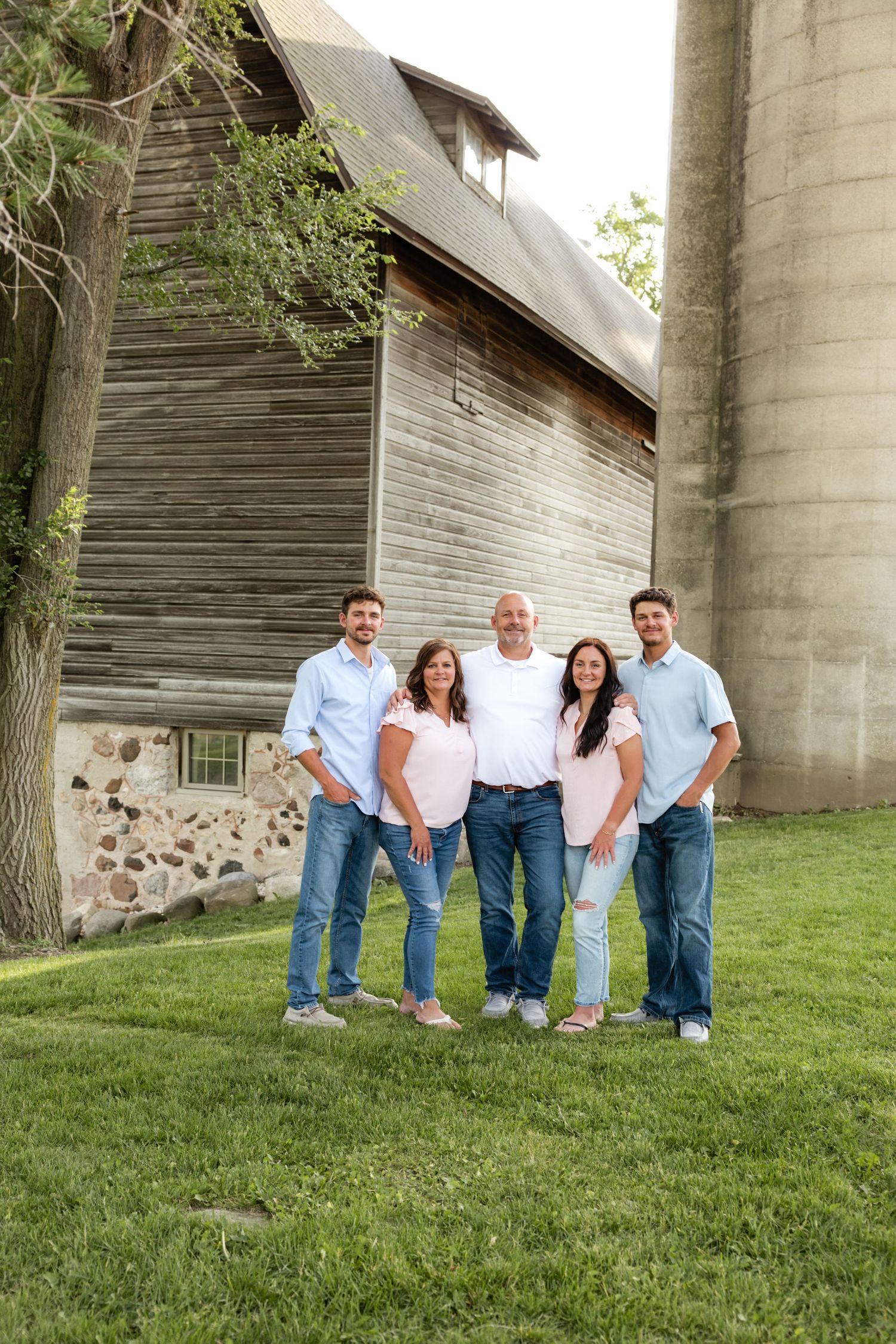 Family group poses casually against rustic concrete wall structure outdoors.
