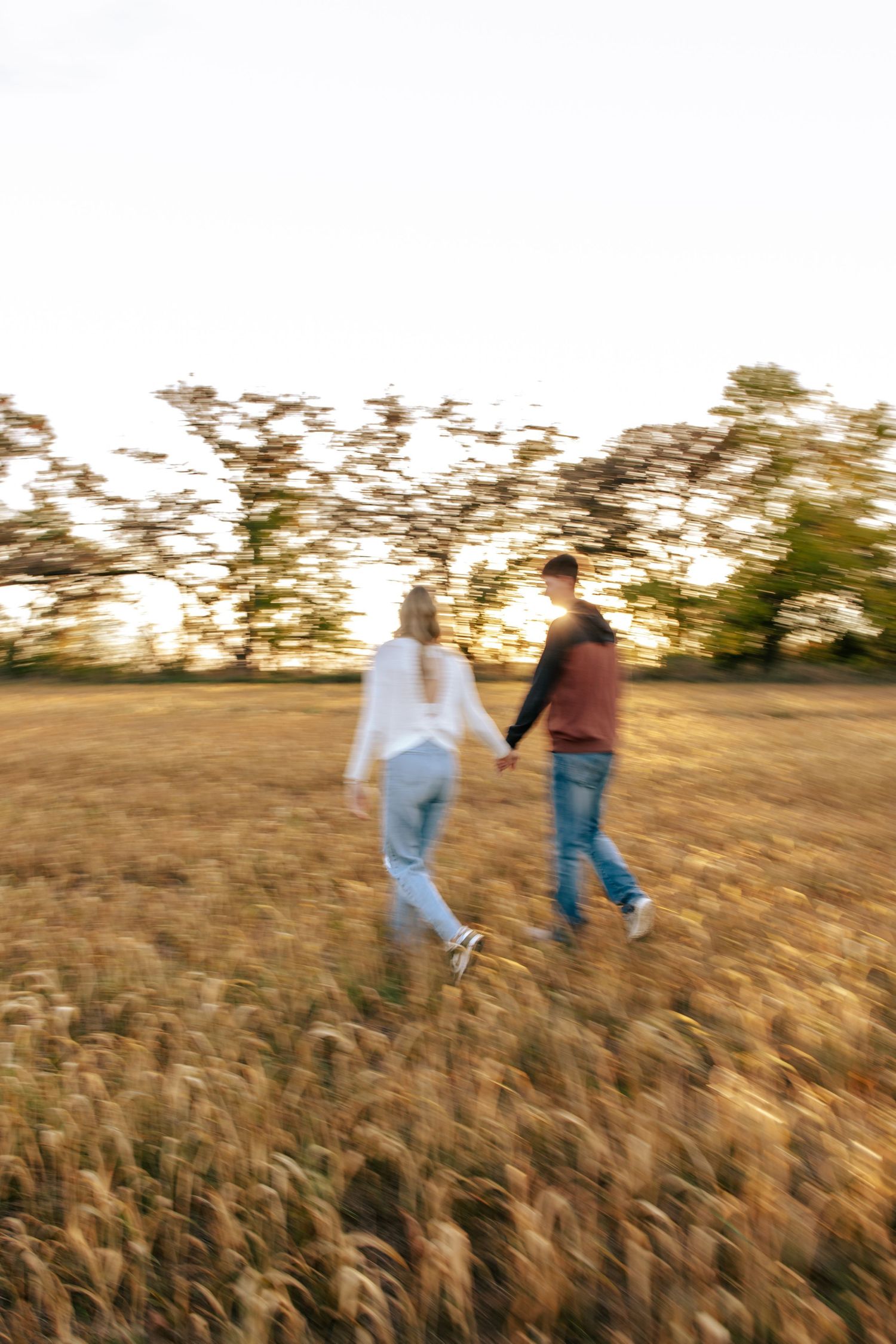 Motion-blurred photo of two people walking hand in hand through a golden field at sunset.