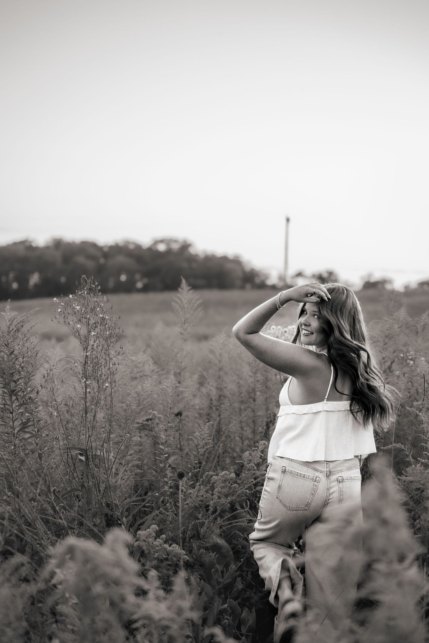 Black and white portrait of woman in white dress standing among wildflowers.