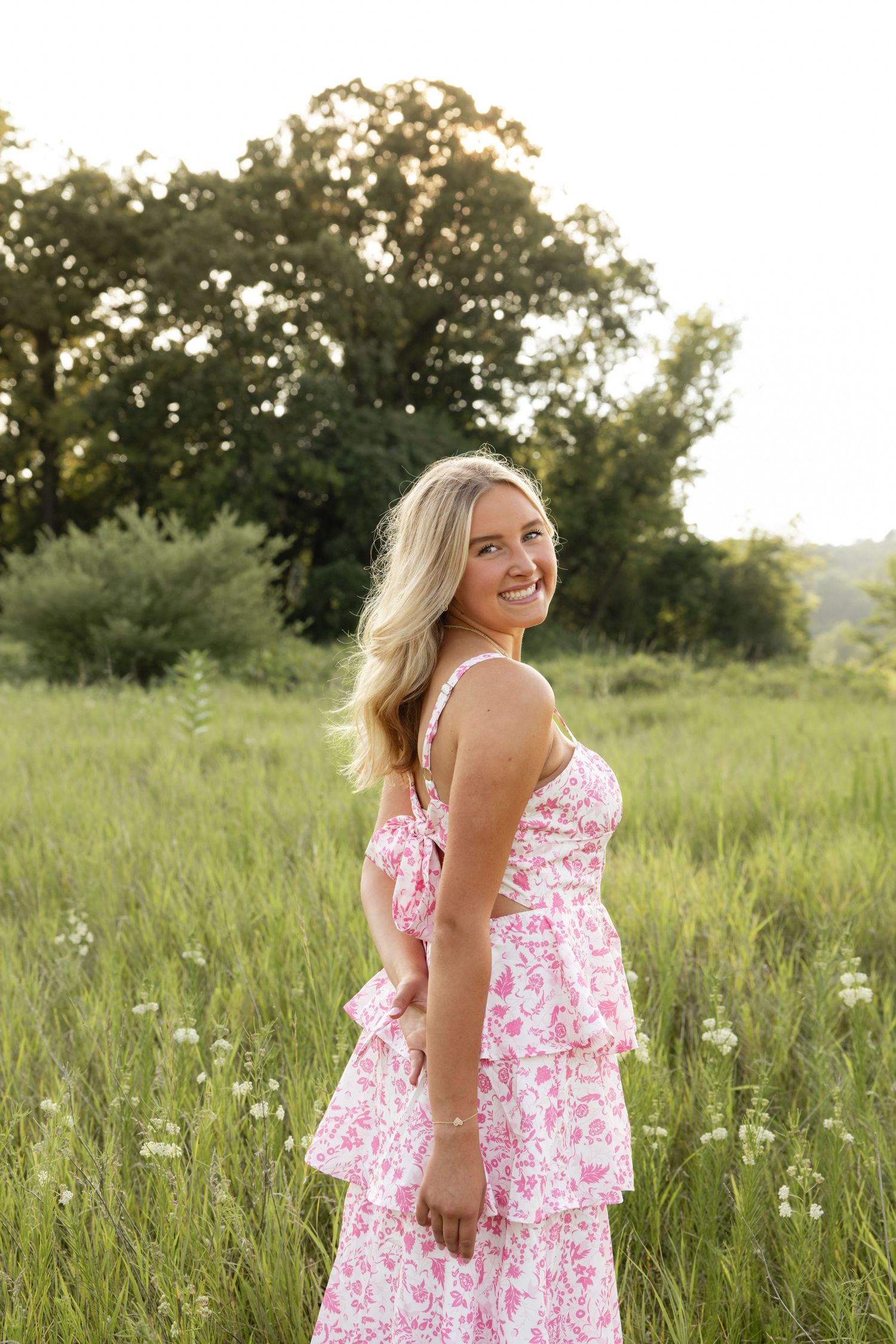Woman in pink floral dress twirling in wildflower meadow during sunset.