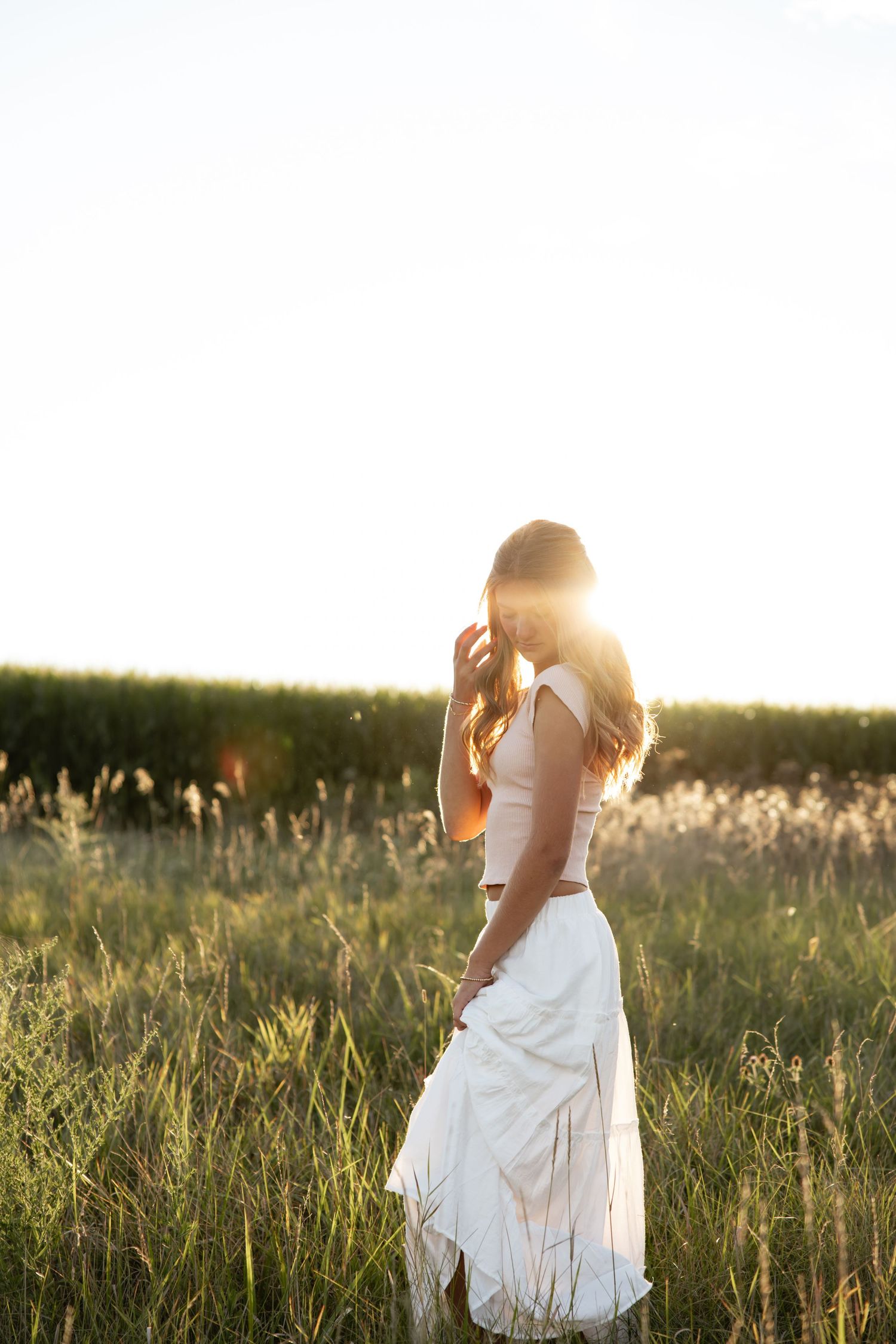 Ethereal sunset portraits in flowing white dress among tall summer grasses.