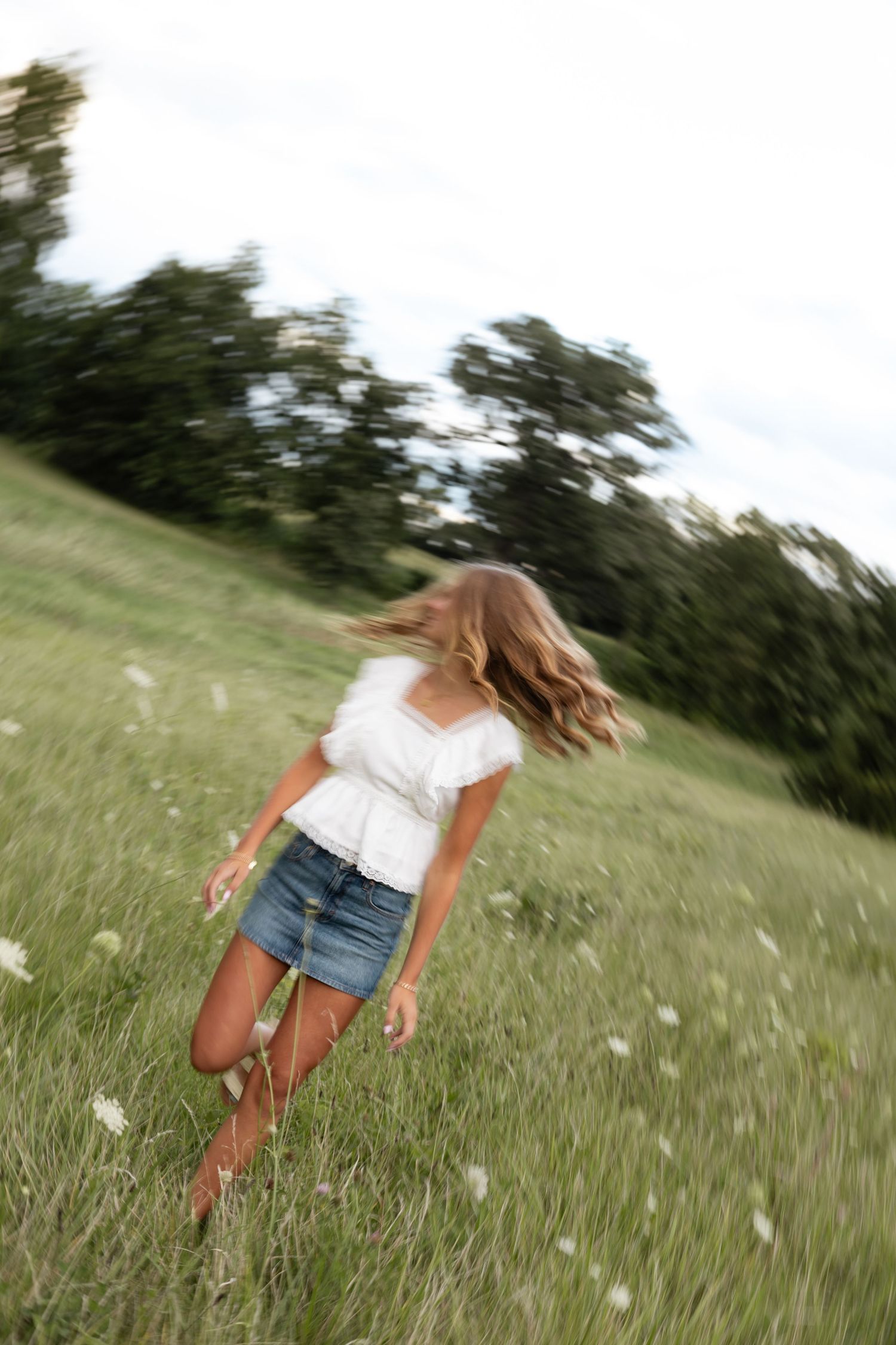 Dynamic motion shots in a breezy meadow with flowing white top and denim shorts.