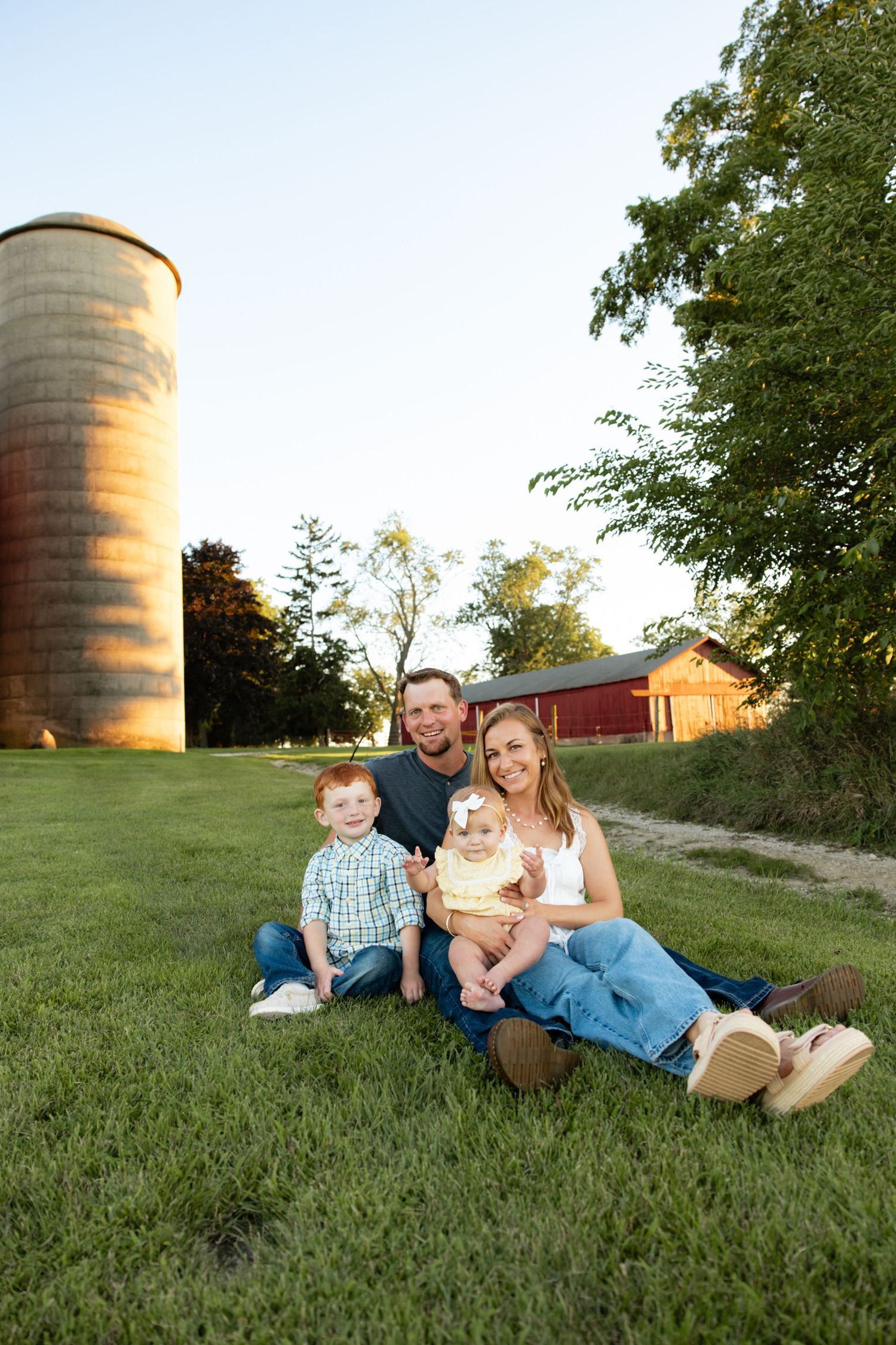 Family resting on grass near rustic farm silo at sunset.