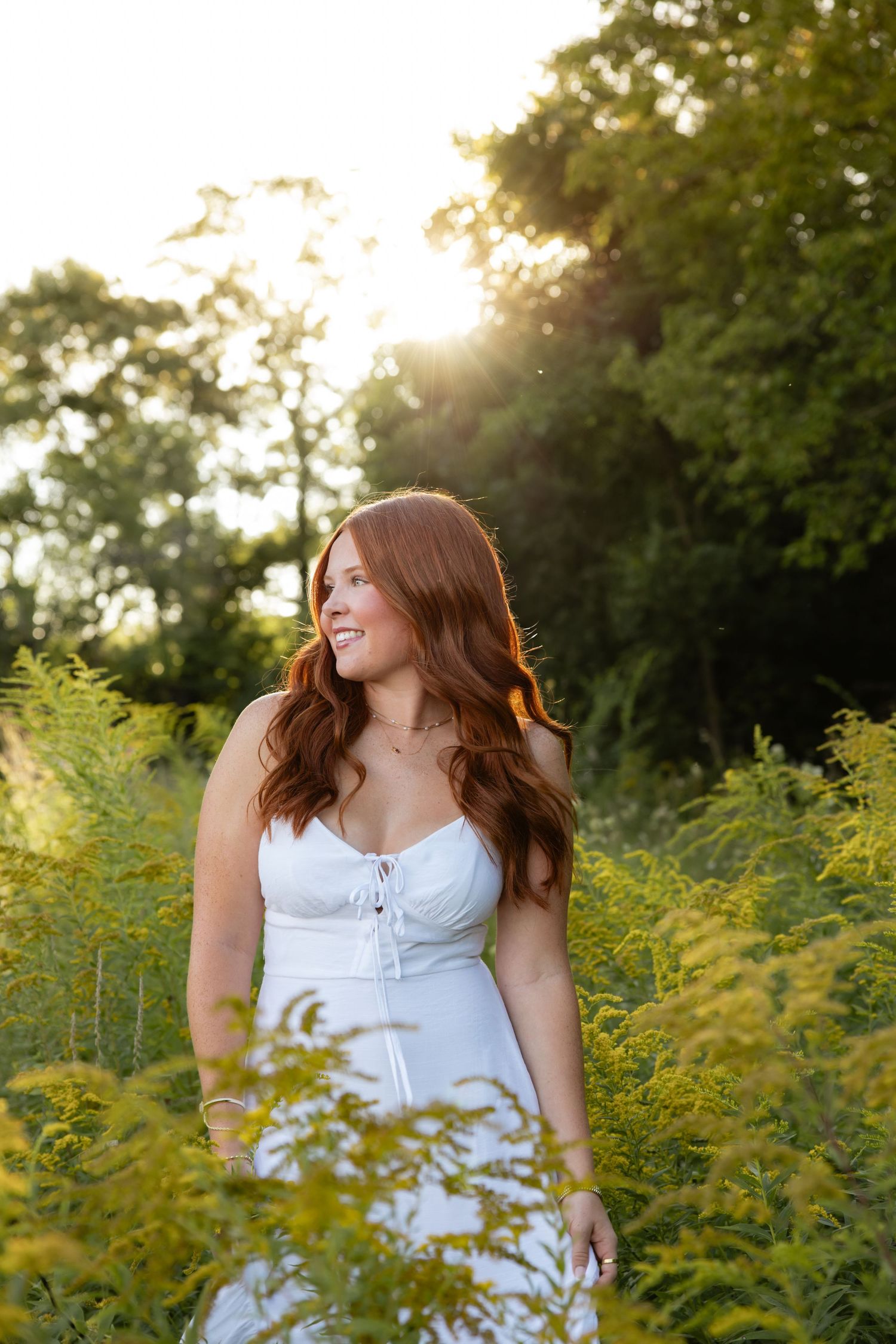 A woman in white dress stands among golden wildflowers during sunset.