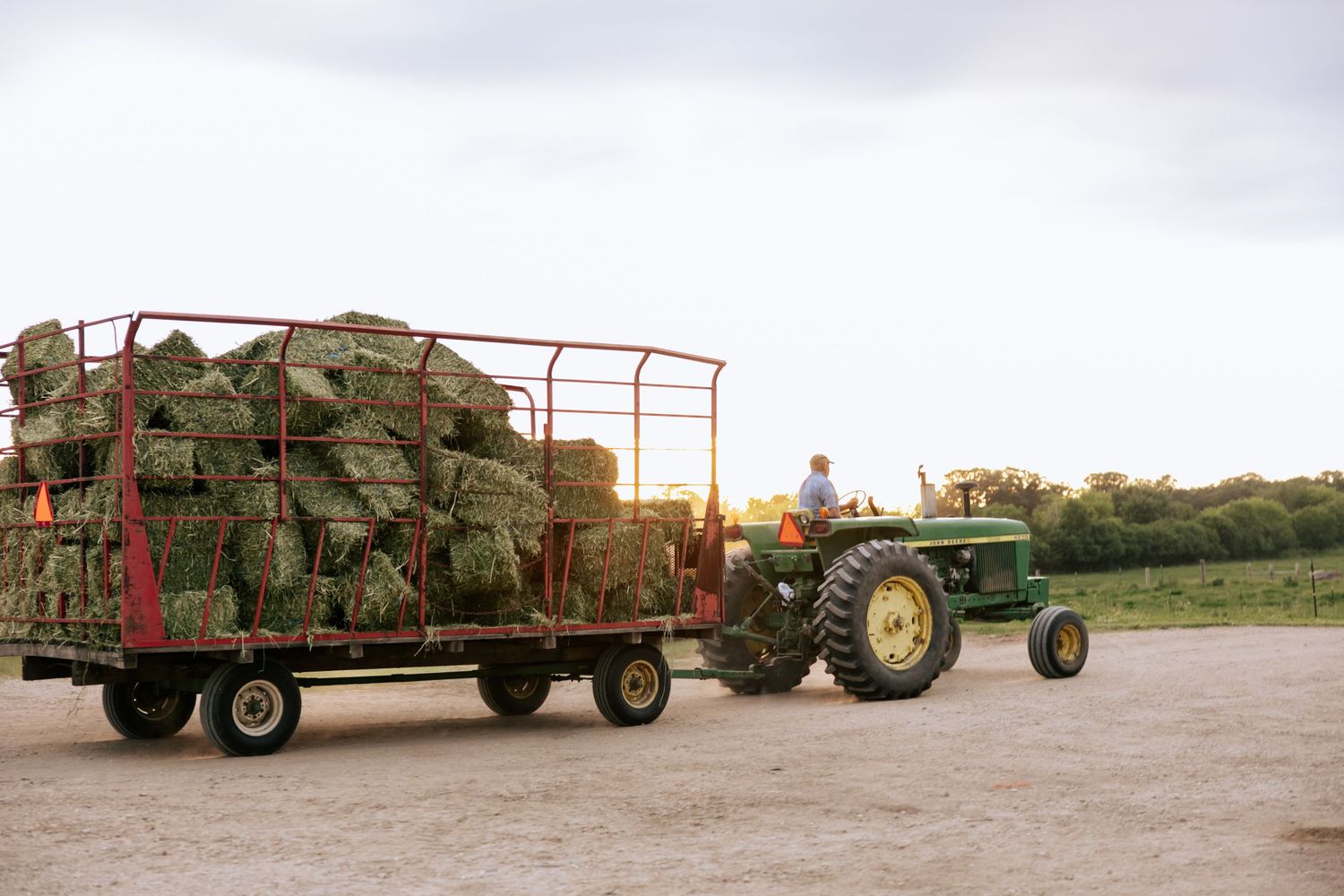 A line of farm equipment and hay bales stretching across a rural field at sunset.