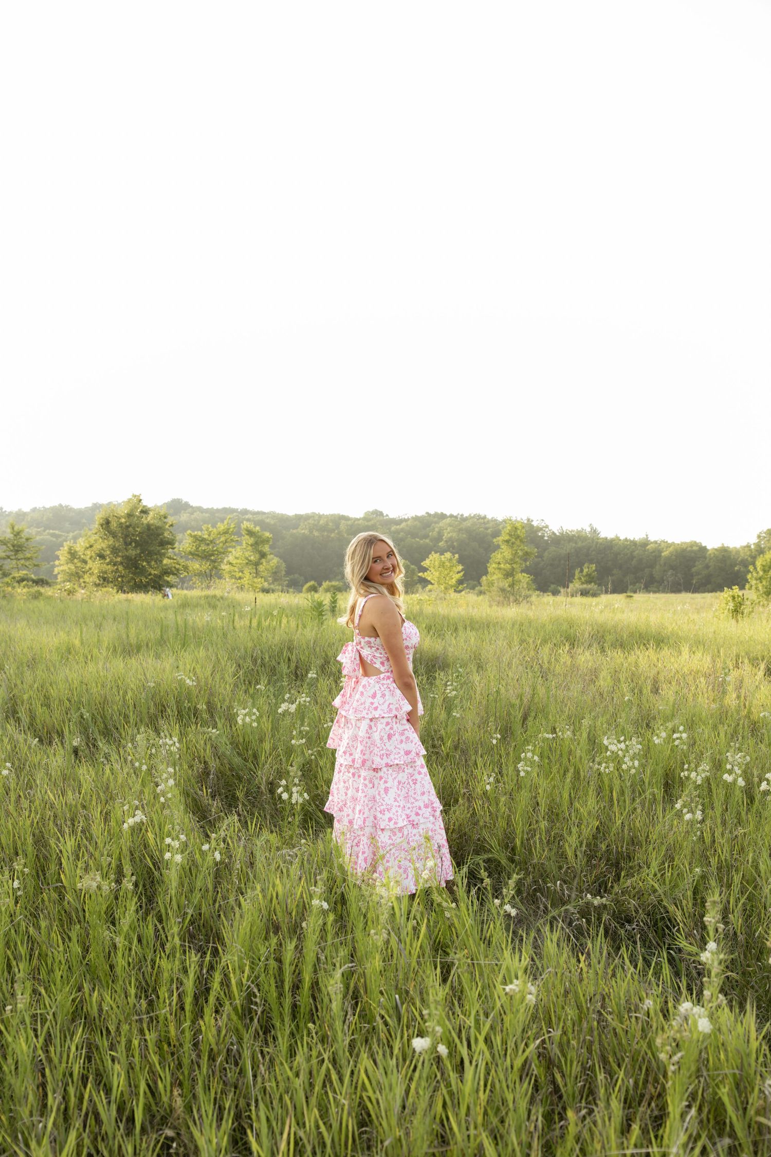Person in pink dress walking through a serene meadow filled with wildflowers.