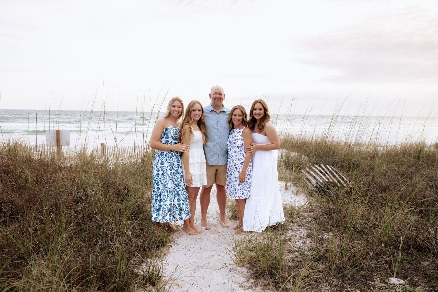 Family gathering on a beach boardwalk wearing coordinated blue and white summer outfits.