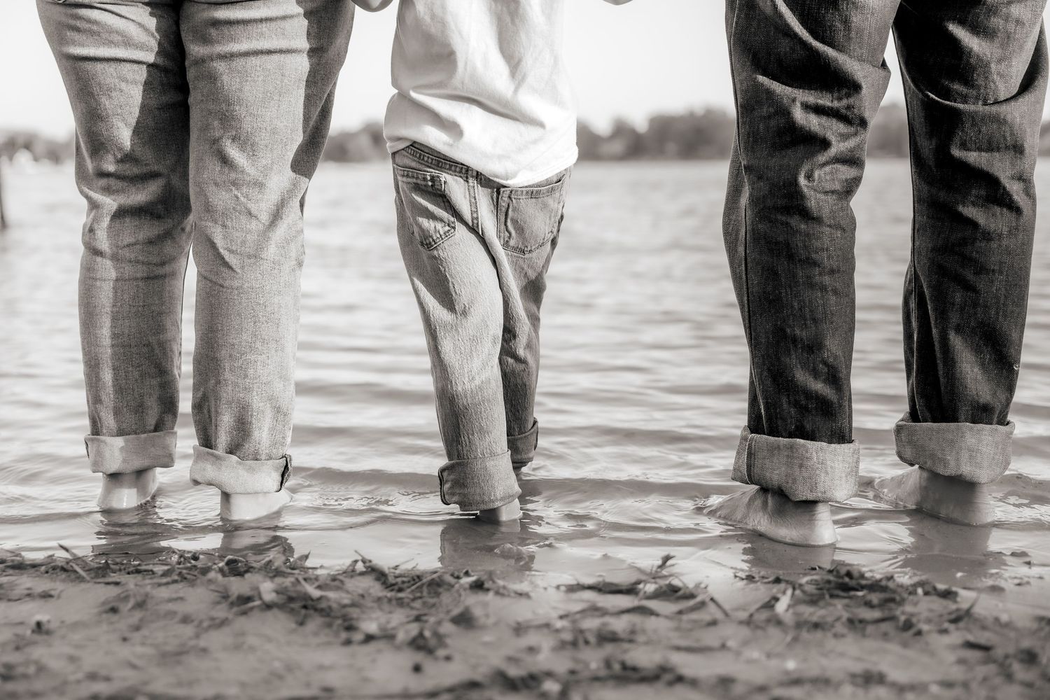 A black and white vintage photograph showing several pairs of legs standing in shallow water at the beach.