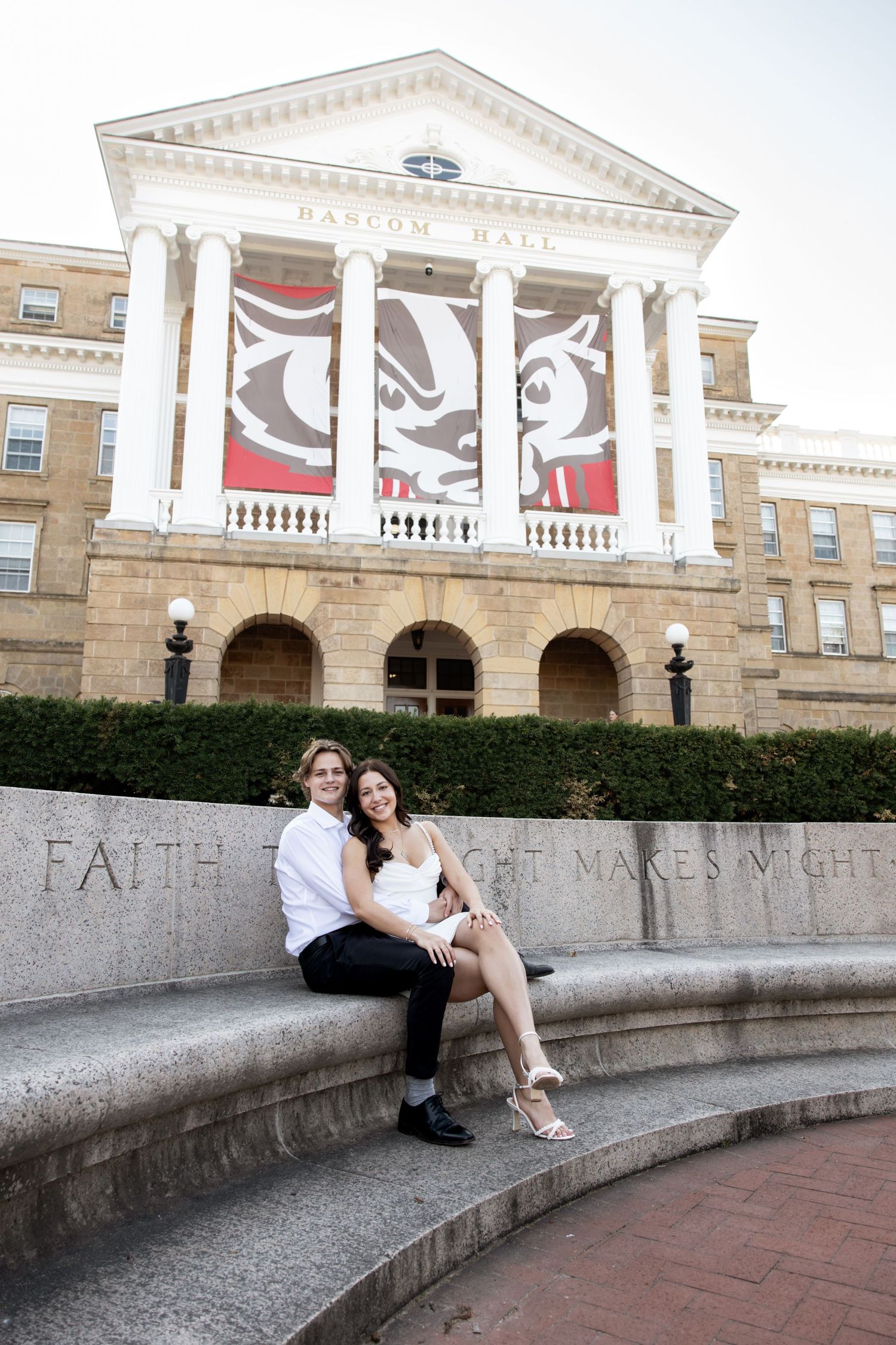 Couple sitting together on stone steps in front of a grand columned building with decorative architectural details.