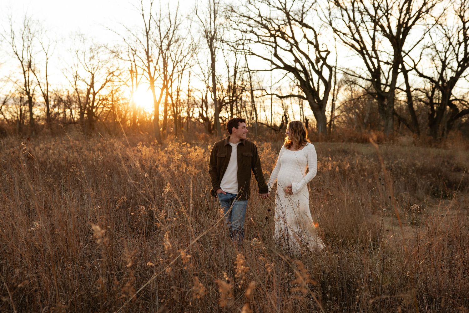 A romantic sunset photoshoot in a golden field with tall grass and bare trees in the background.
