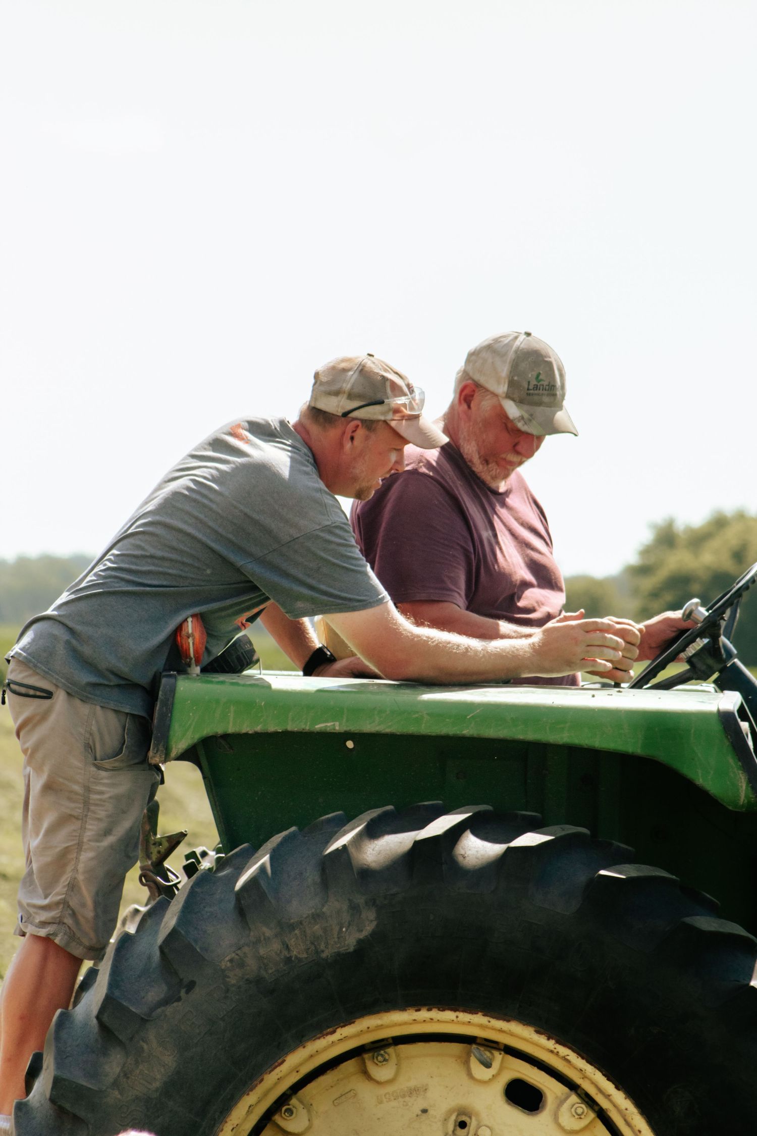 Farm workers inspecting and maintaining a large green agricultural machine in a field.