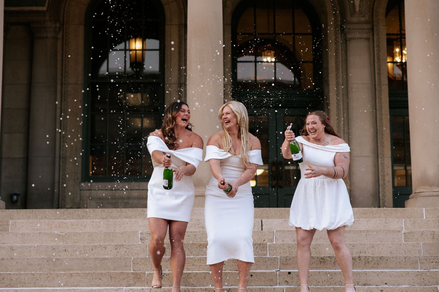Group of graduates in white dresses posing together on outdoor stone steps.