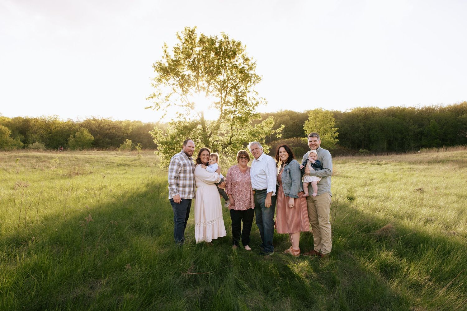 Family portrait session in an open field during sunset with coordinated outfits.