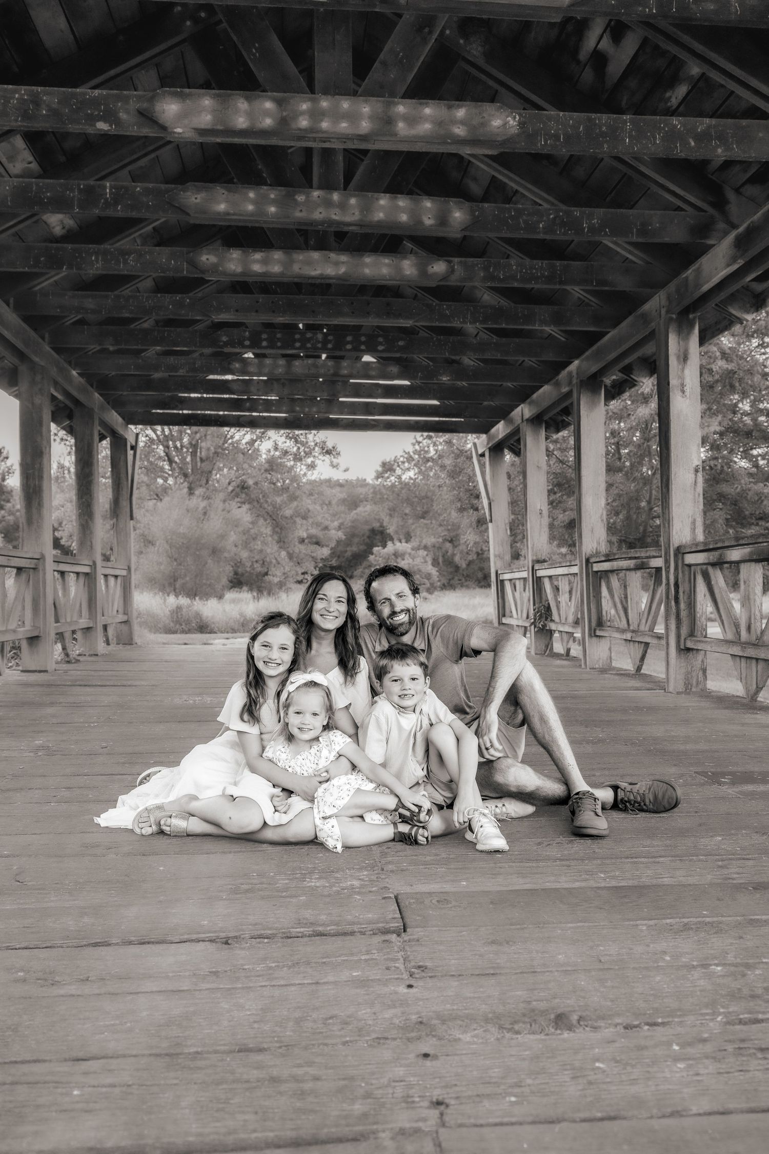 Black and white portrait of a family sitting together on a covered wooden bridge.