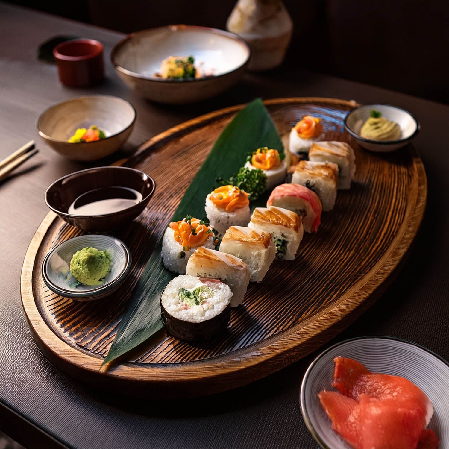 Selezione di sushi artigianale servita su taglieri di legno con salse da immersione e guarnizioni.