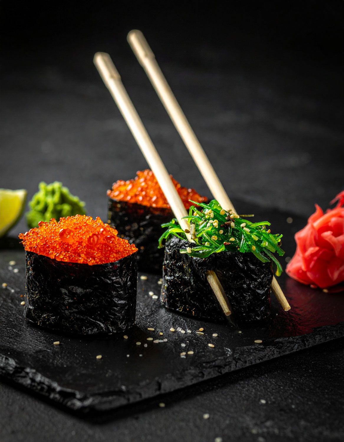 Sushi gunkan con uova color arancio brillante e alga, servito su ardesia nera con bacchette.