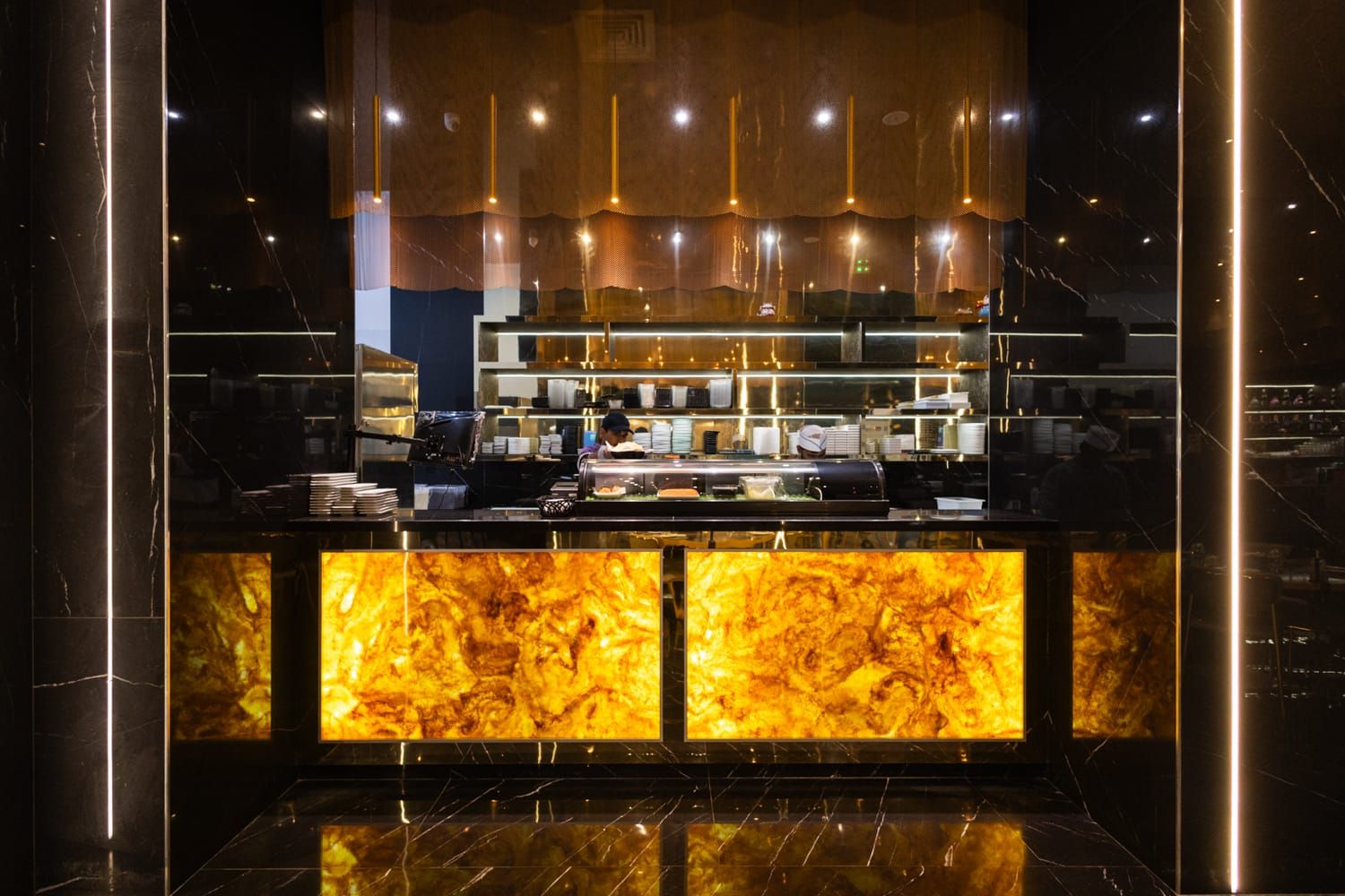 Un moderno bancone bar illuminato da pannelli retroilluminati in onice ambrato nella sala a Trapani di Roku Sushi Restaurant.