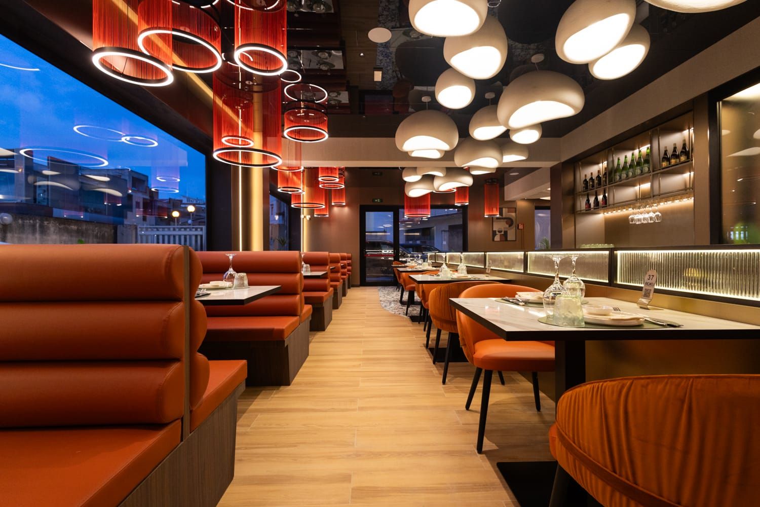 Interno del ristorante Roku Sushi Restaurant con divanetti in pelle arancione e lampade a sospensione a Barcellona Pozzo di Gotto, Sicilia.