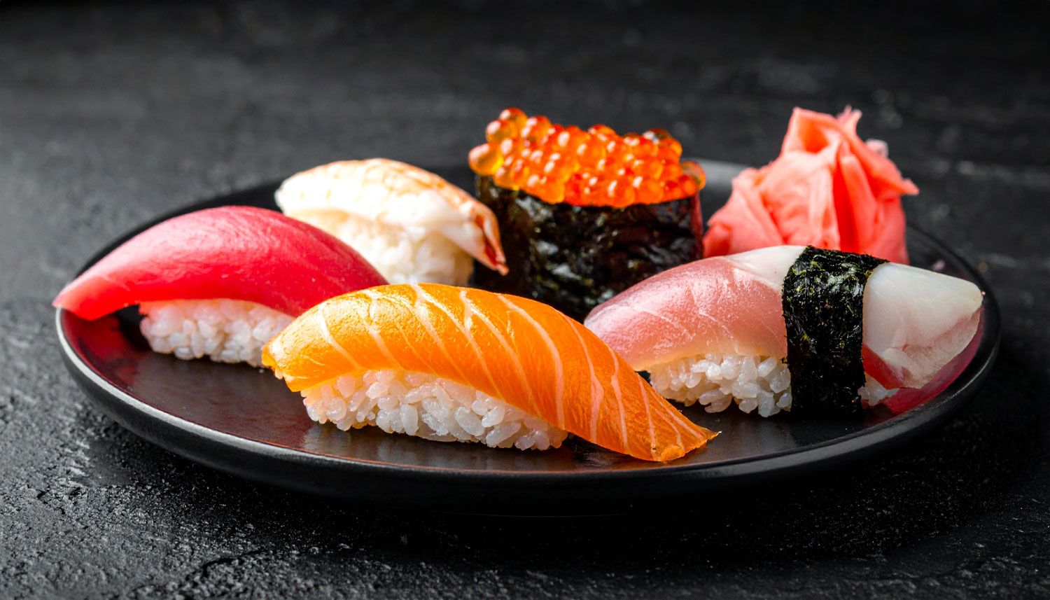 Pezzi di sushi nigiri freschi con salmone e tonno disposti su piatti scuri con guarnizioni.