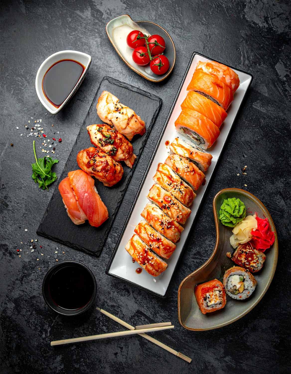 Varietà di roll colorati e antipasti presentati ad arte su vassoi di pietra scura.