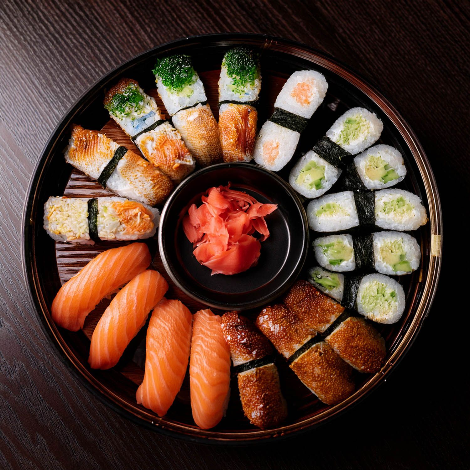 Grande vassoio di sushi con nigiri al salmone e vari roll disposti su una superficie di legno scuro.