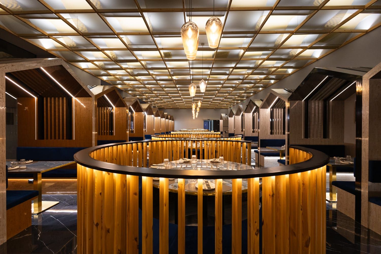 Sala di Roku Sushi Restaurant a Trapani, in Sicilia, con pareti a doghe di legno e lampade geometriche a soffitto con tavoli tondi.