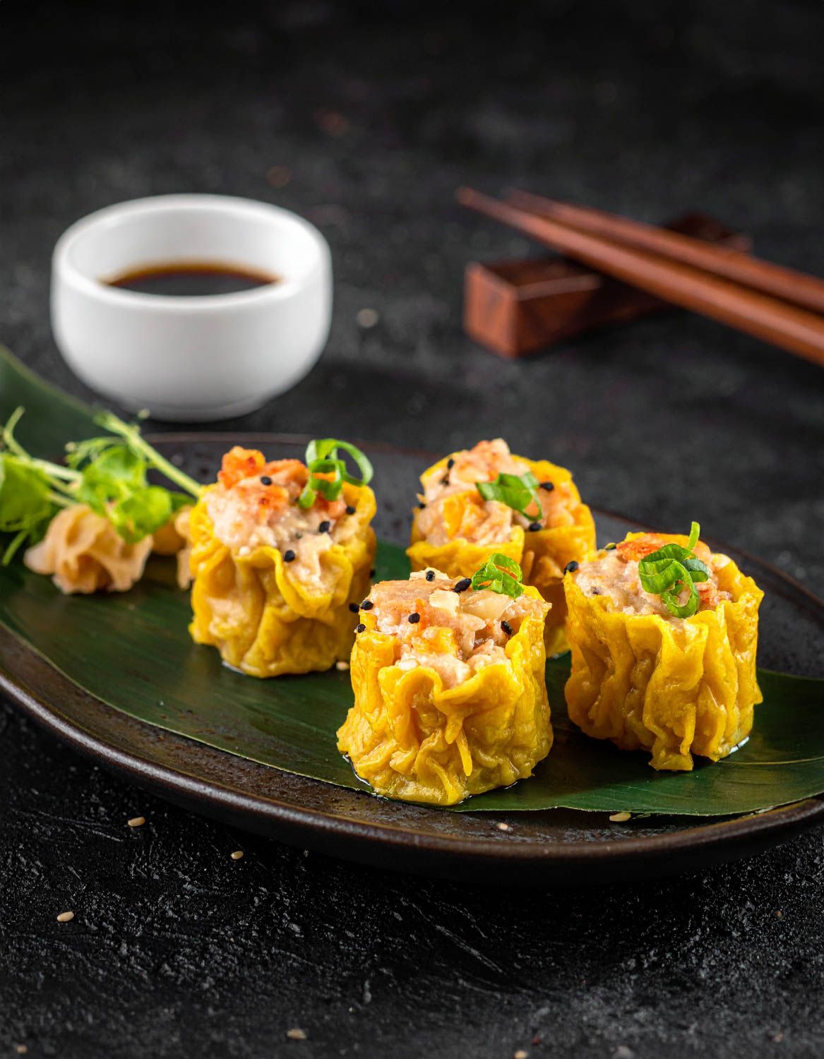 Ravioli shumai tradizionali guarniti con uova e erbe, serviti su piatti scuri con salsa da immersione.